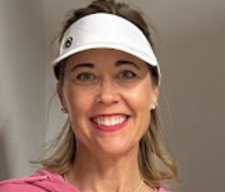 A smiling woman wearing a white visor and pink sports jacket.