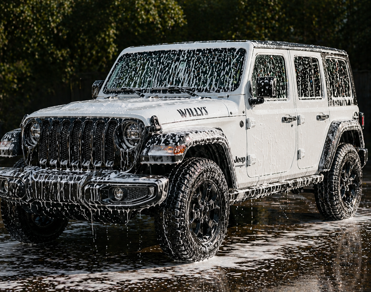A white Jeep Wrangler with black wheels is covered in soap suds and foam, sitting in a shallow puddle outdoors with trees in the background.