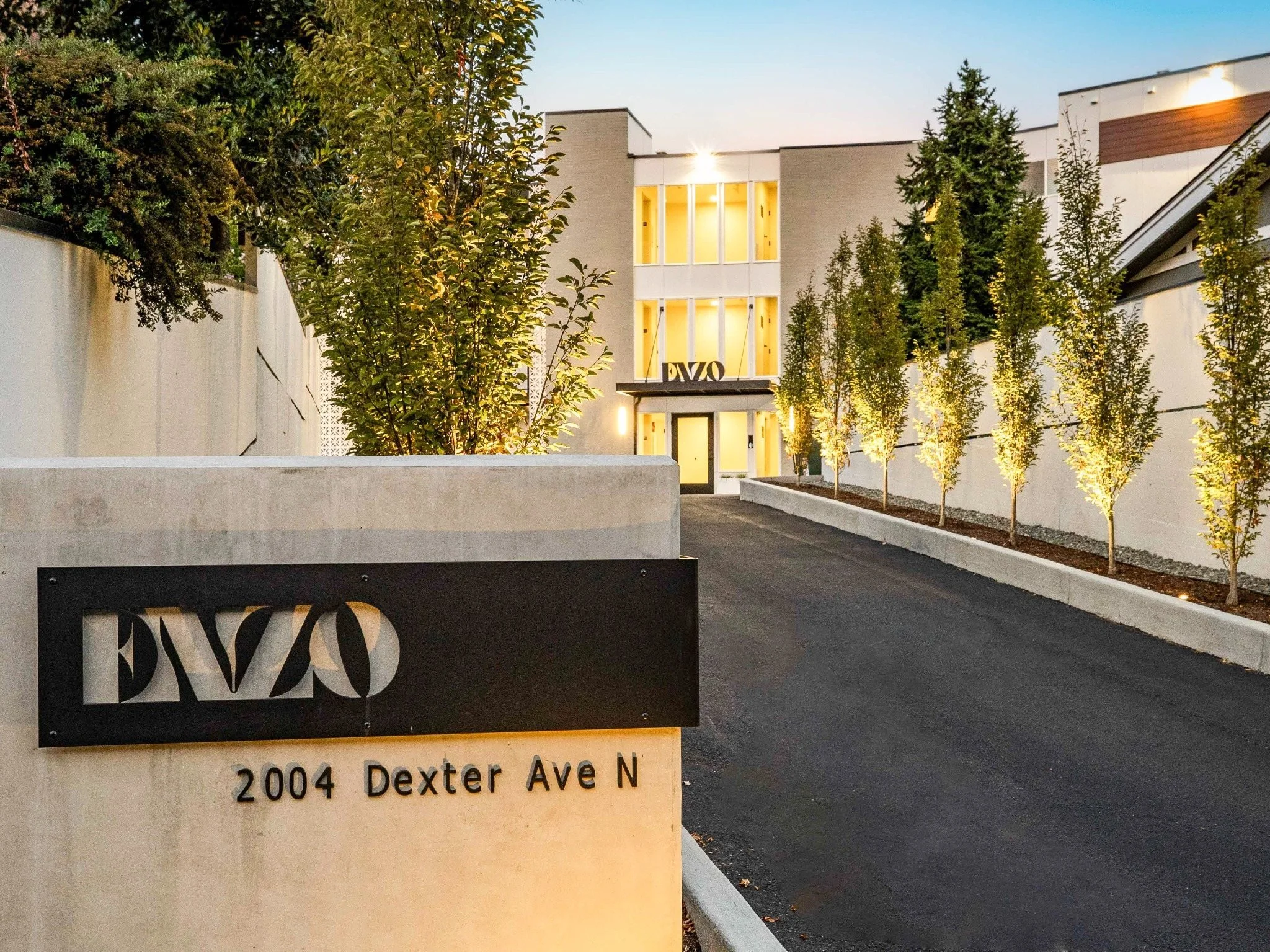 Modern building with illuminated windows, trees along the sidewalk, and a street sign that reads "2004 Dexter Ave N."