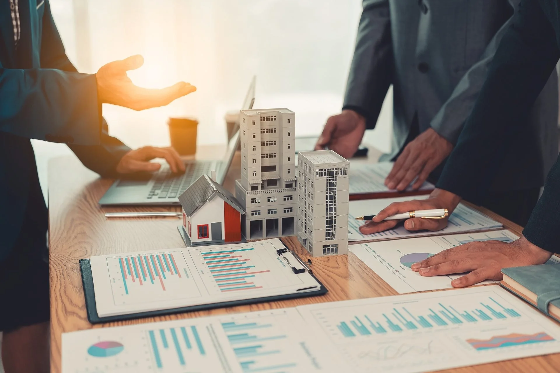 Business professionals discussing architectural models of buildings at a meeting table with charts and documents.