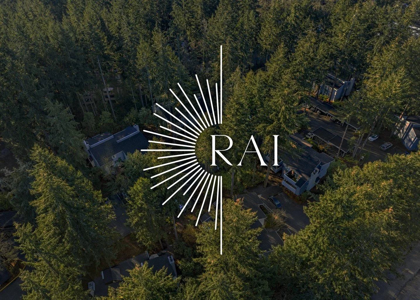 Aerial view of a forested neighborhood with houses and trees, with a white logo in the center that says 'RAI' surrounded by radiating lines.