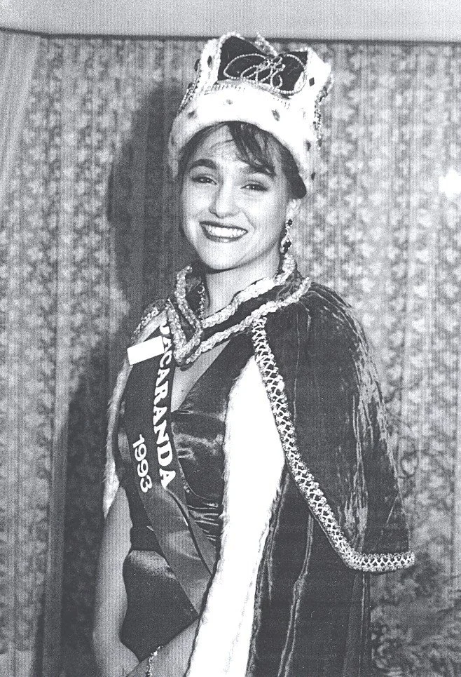 Young woman wearing a crown, sash reading "Hawaii Island 1993," and evening gown, smiling, against a curtain background.