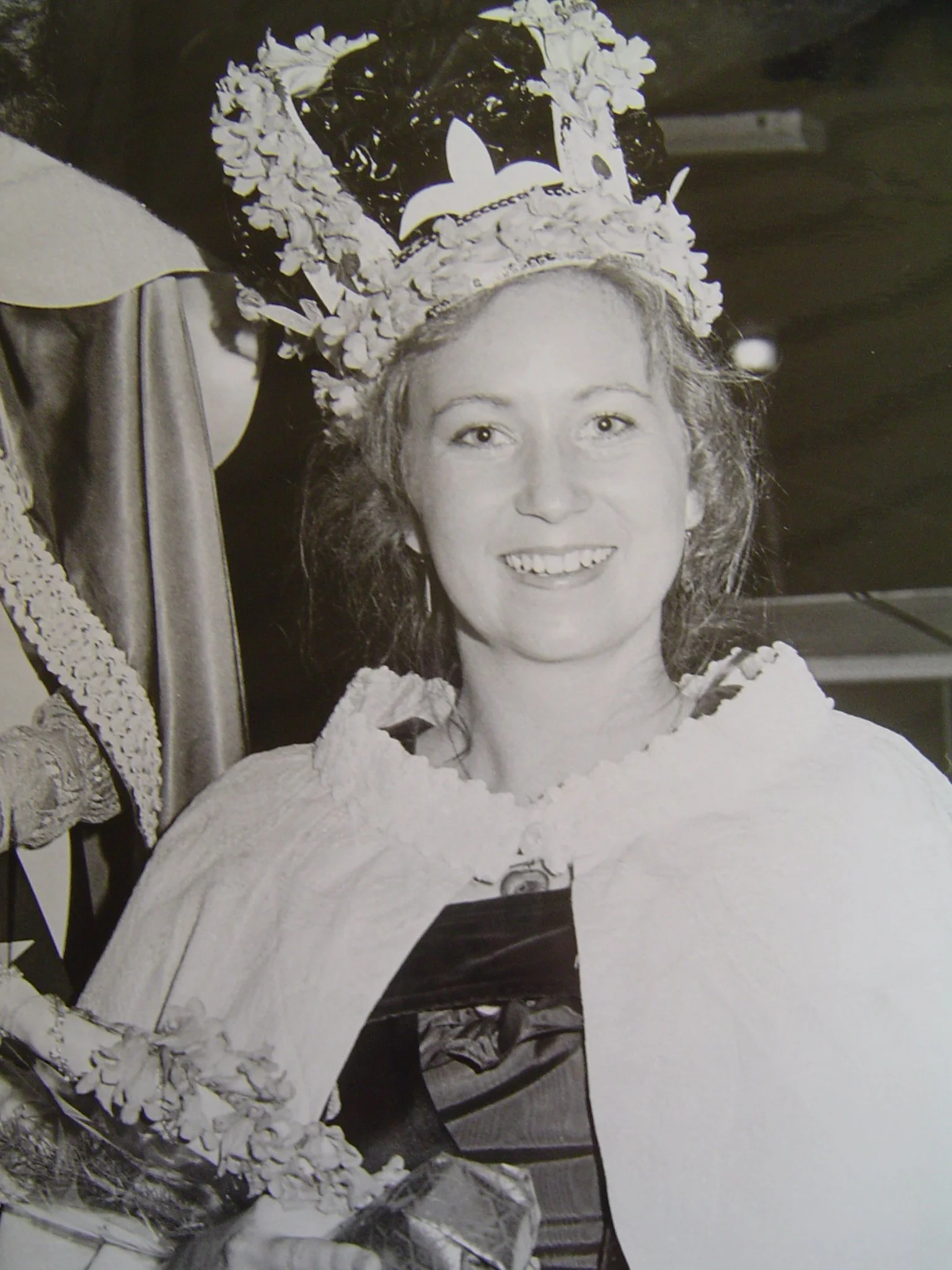 A woman wearing a crown decorated with flowers and a dress, smiling at the camera.