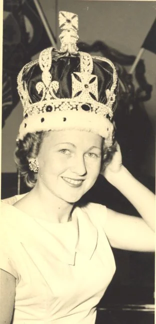 A woman smiling while wearing a large ornate crown.