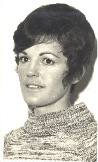 A black and white portrait of a woman with short, dark hair wearing a knitted turtleneck sweater.