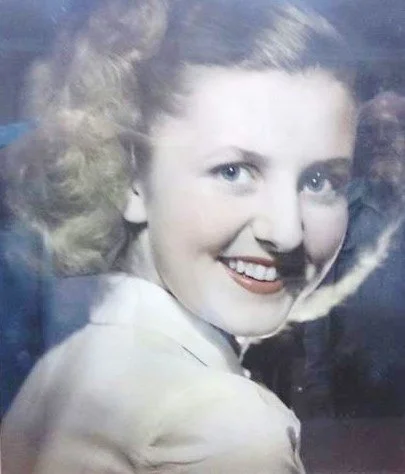 A woman with light-colored hair smiling at the camera, wearing a light-colored top.