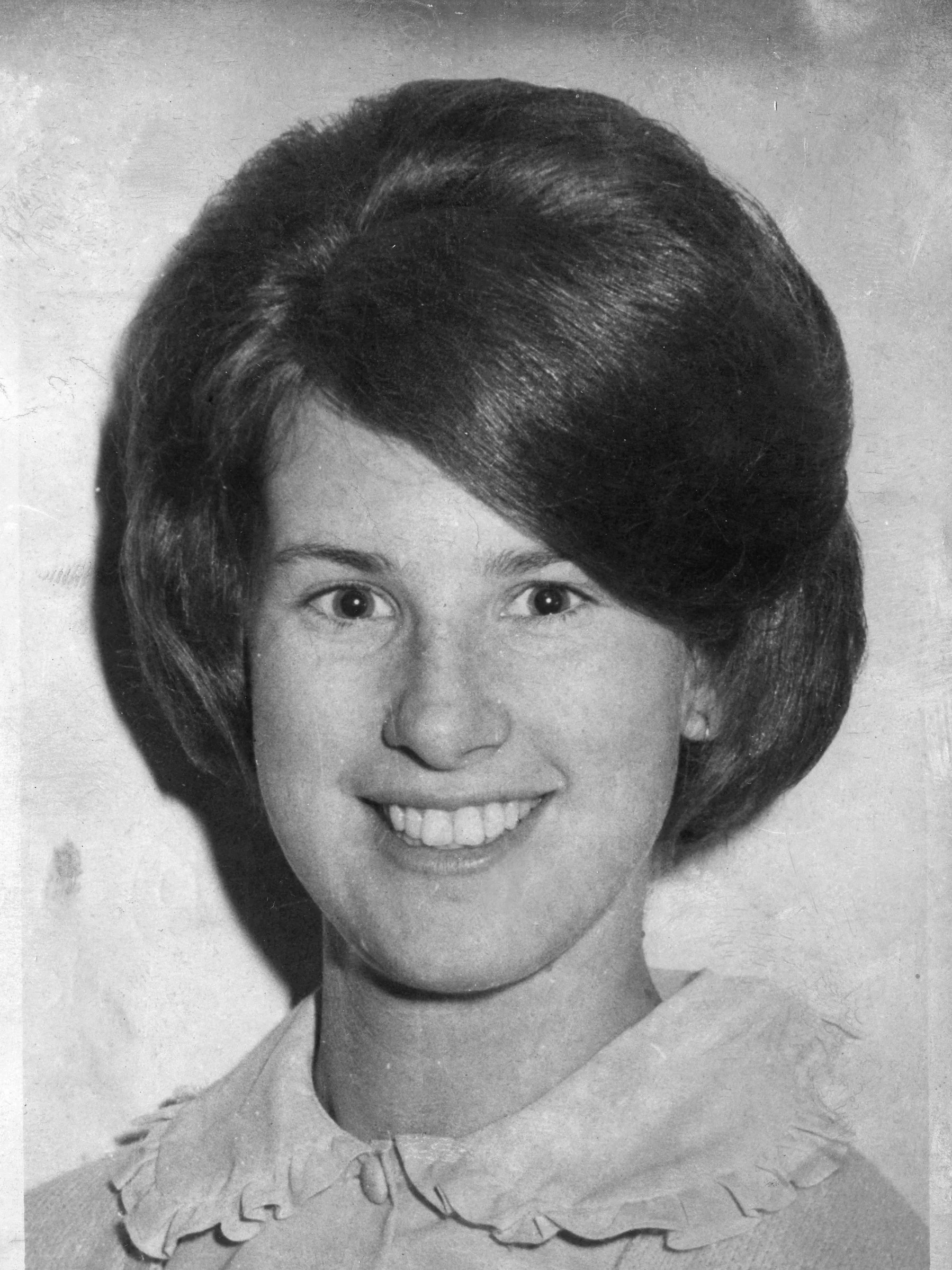 Black and white vintage photograph of a woman with a big smile, short layered hairstyle, wearing a dress with a ruffled collar and a necklace.