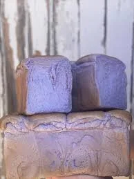 A close-up of three blocks of lavender soap stacked on top of each other against a blurred background.