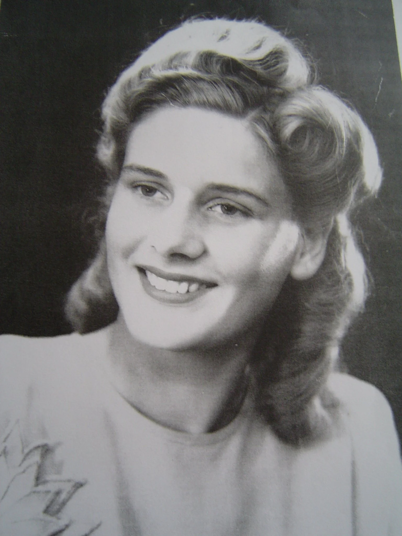 Black and white photograph of a smiling woman with wavy, styled hair.