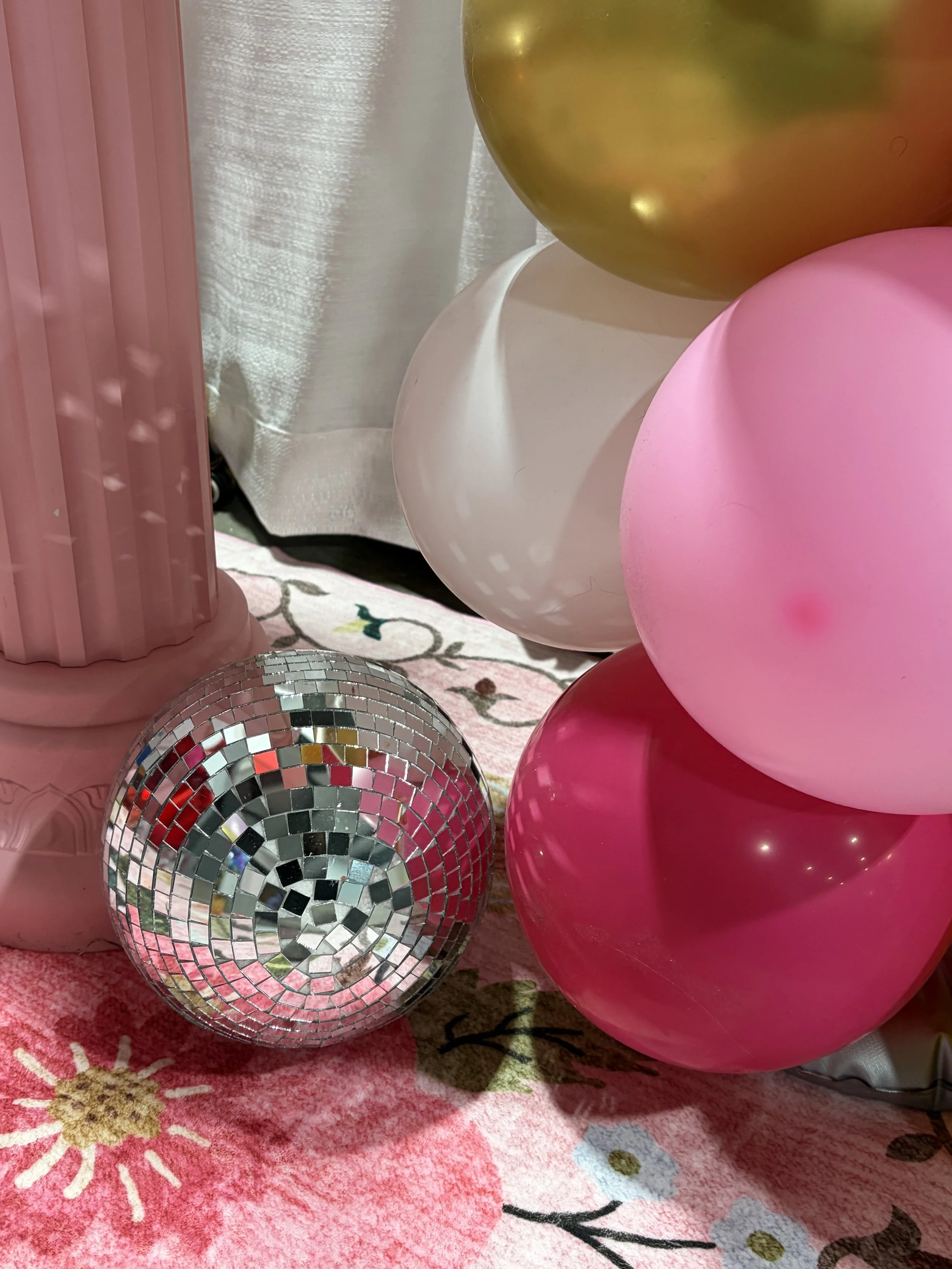 Pink, white, gold, and red balloons on pink floral-patterned carpet with a mirror ball.