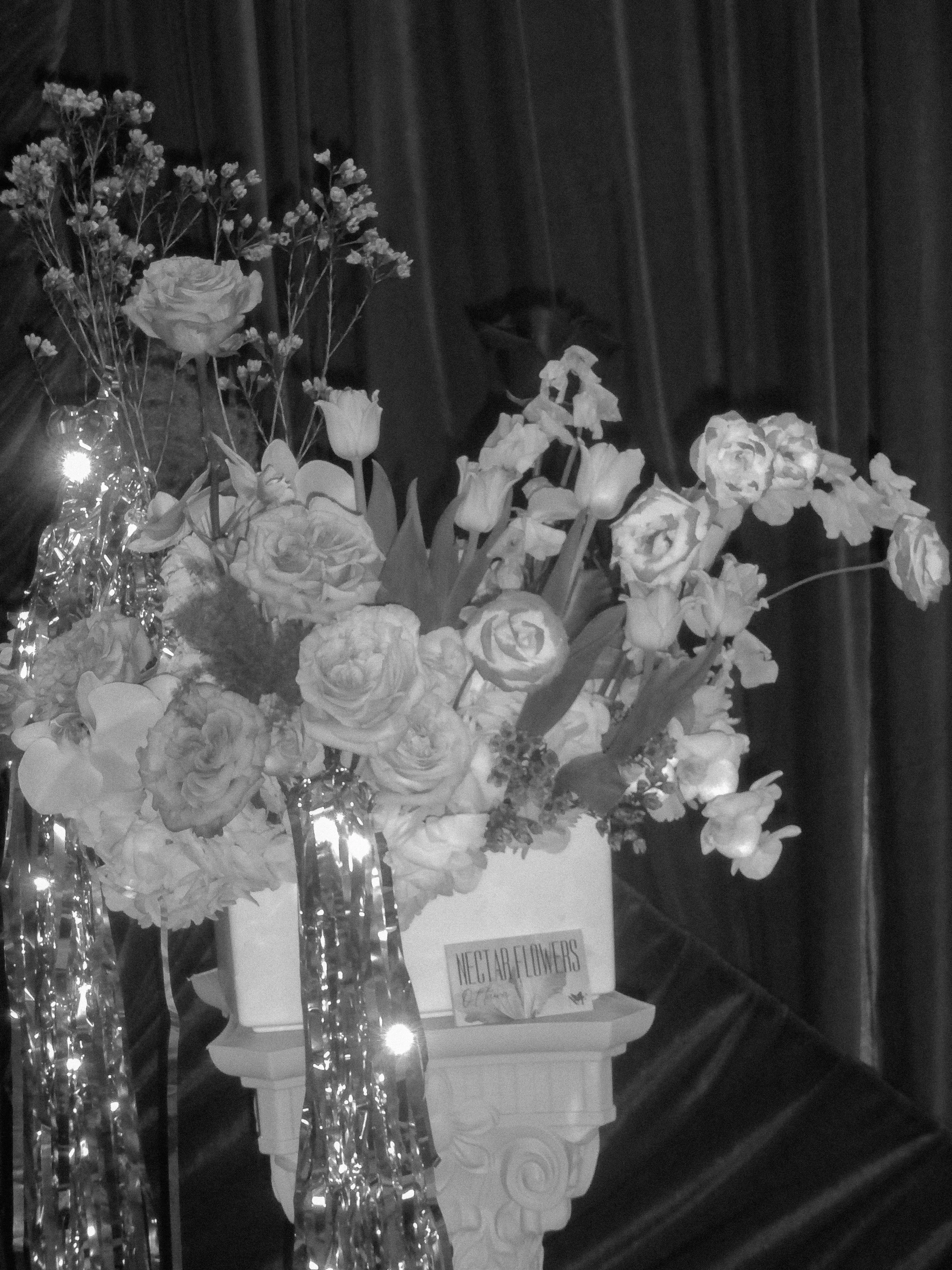 Arrangement of various flowers in vases, including roses and tulips, on a table with a 'Next a Flower' sign.