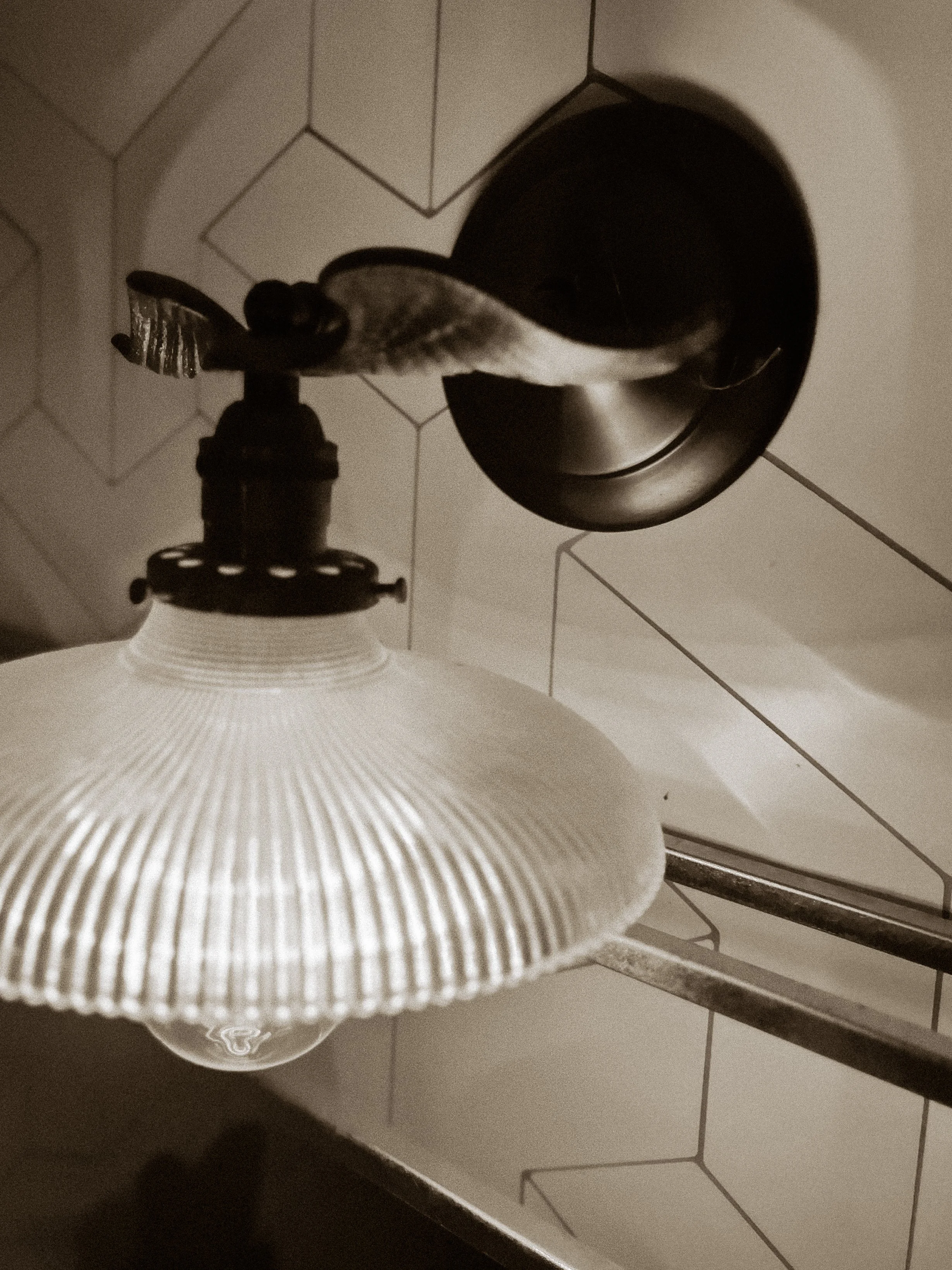 Close-up of a hanging ceiling light fixture with a textured white glass shade and metal hardware, against a tiled wall.