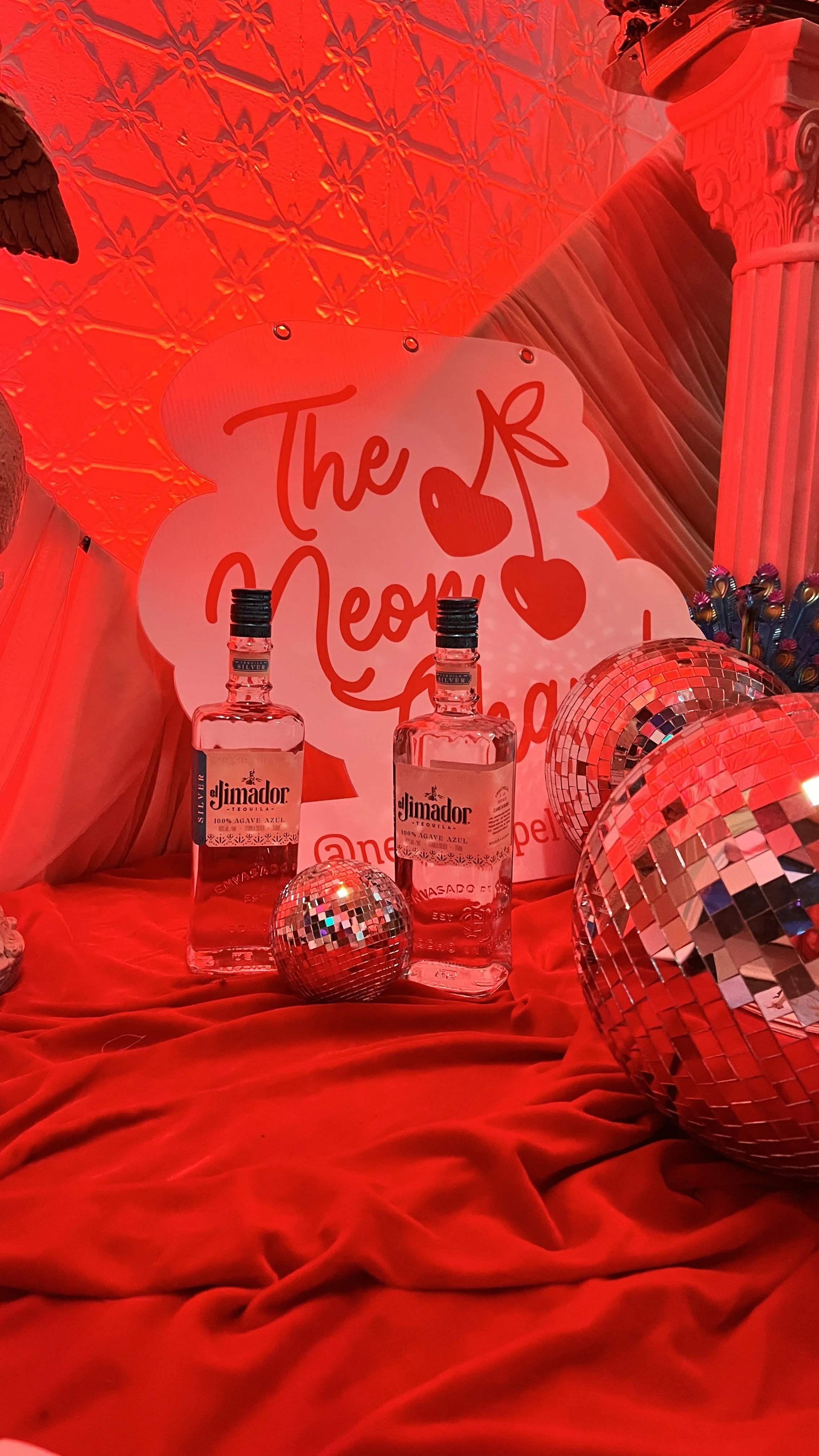 Display with bottles of El Jimador tequila, a sign with cherries and text, disco balls, and red decor, indicating a festive or celebratory setup for a disco themed wedding.
