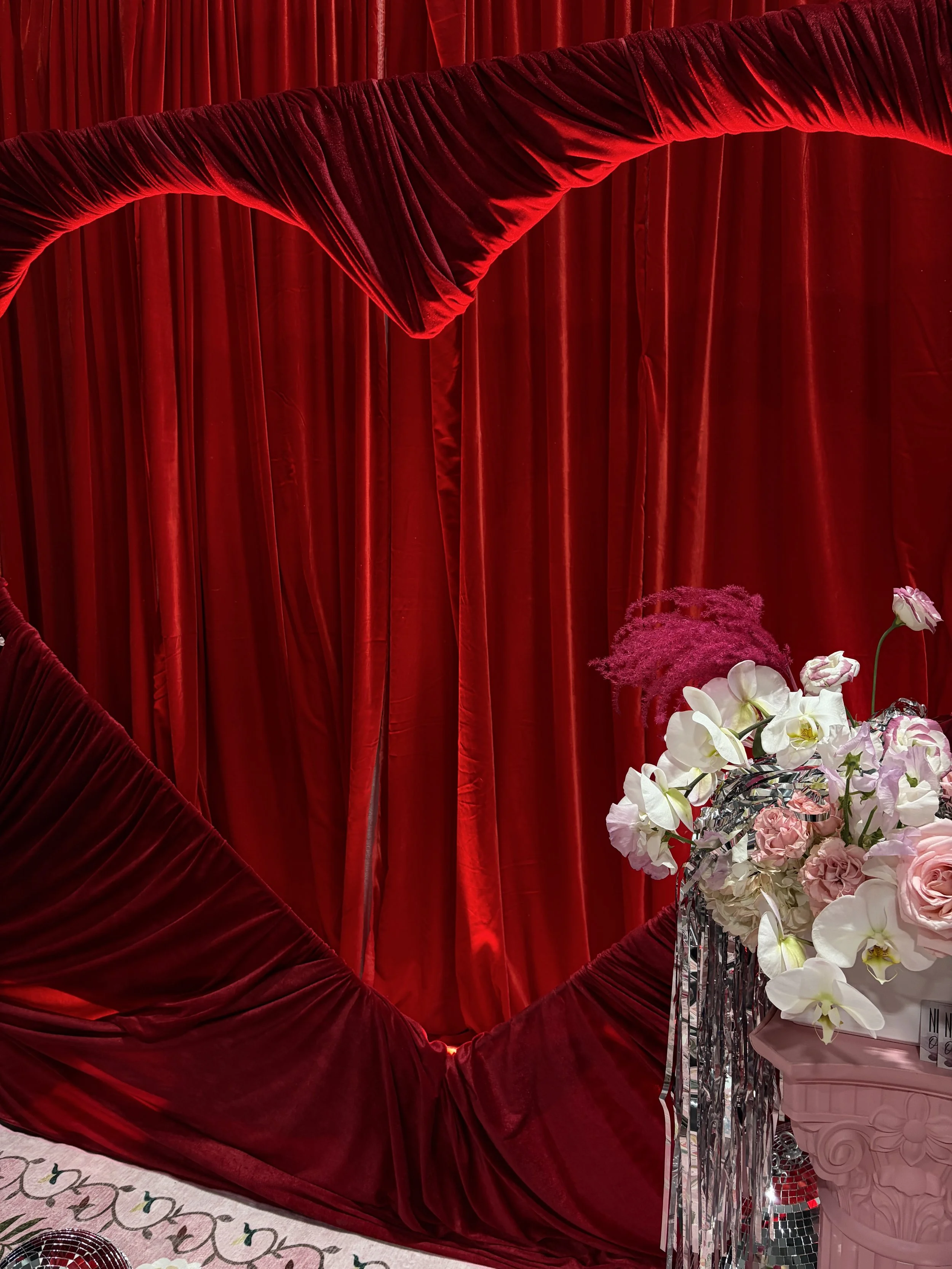 Red velvet curtain with floral arrangements in a silver vase on a decorative table.