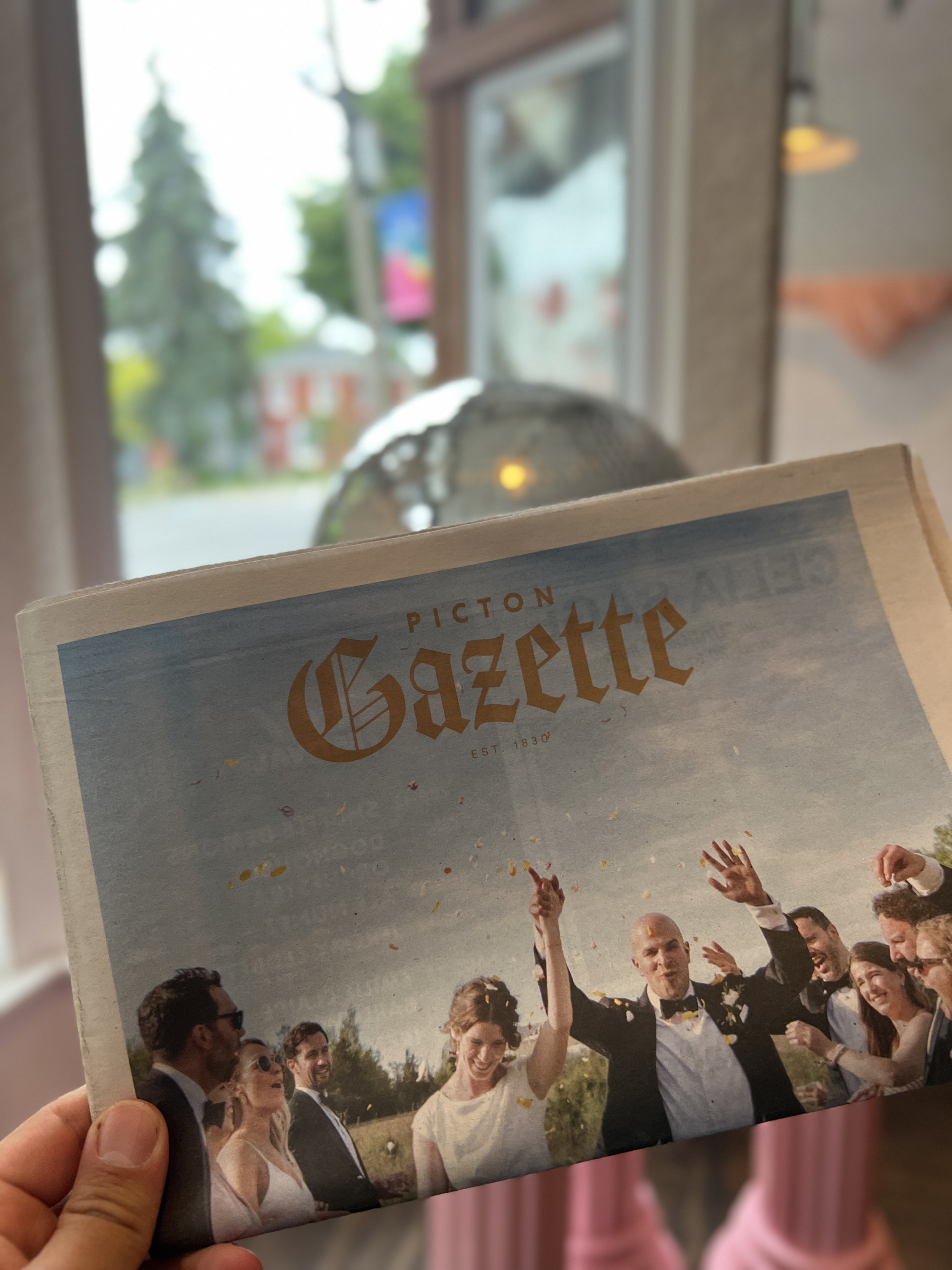 A person holding a wedding magazine with a cover photo of a happy bride and groom celebrating outdoors with friends.