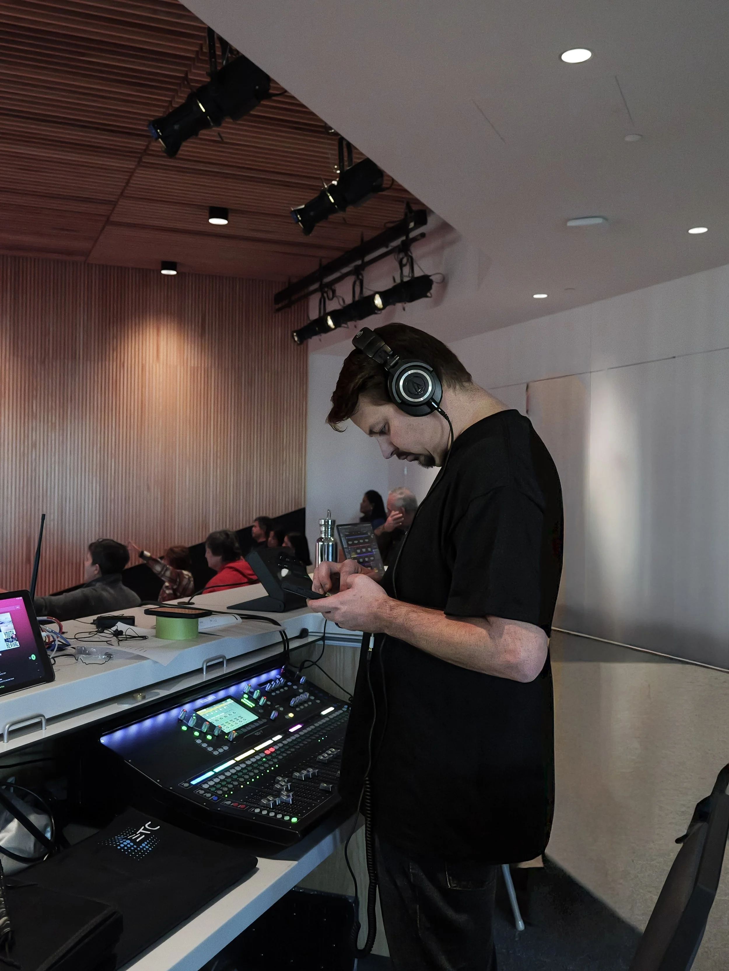 Man using electronic music equipment in a family church in Woodbury, wearing headphones, with audience members seated in the background.