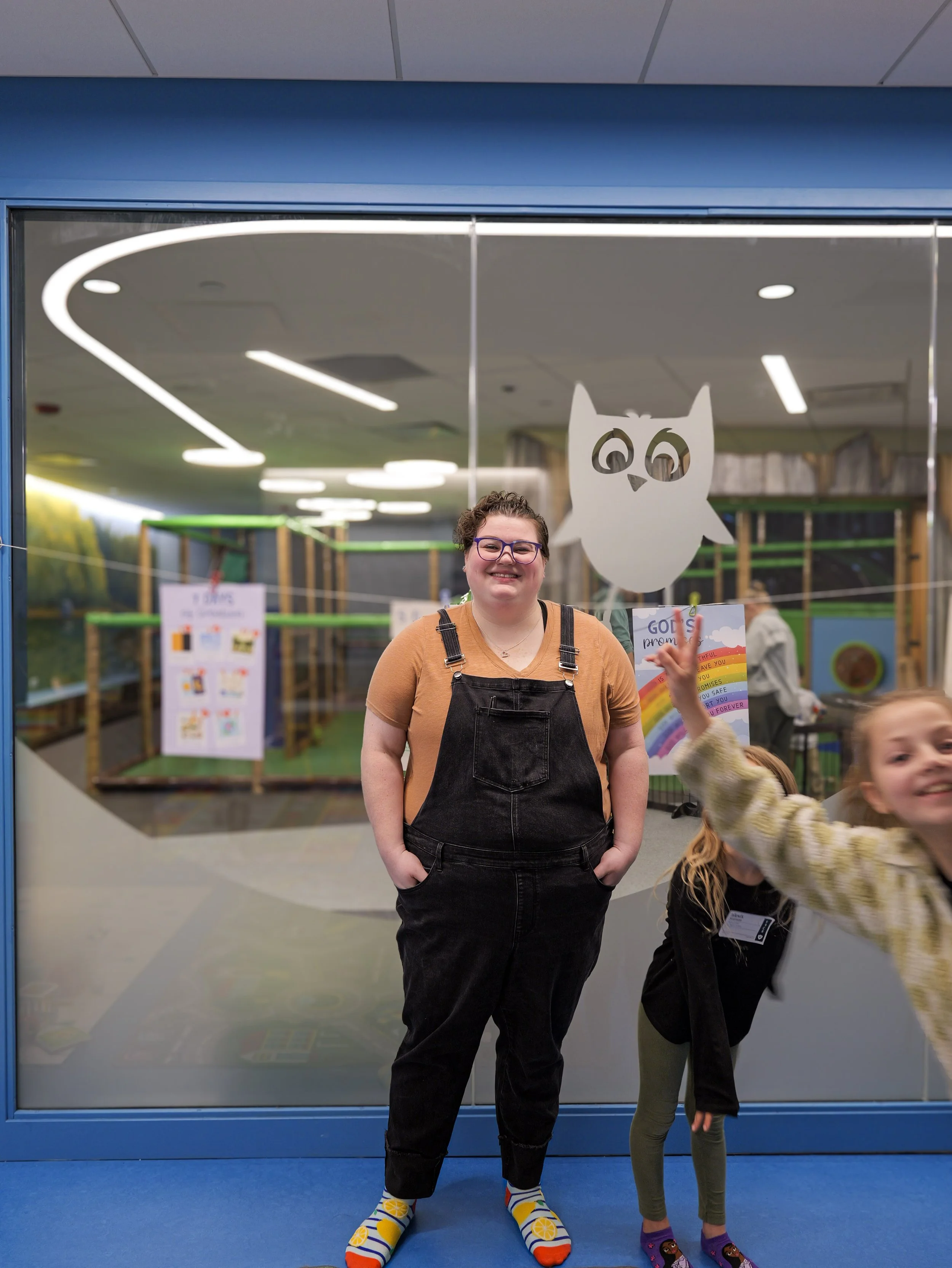 A smiling kids pastor standing in front of an indoor playground. Smiling and jumping children at a family church in Minnesota with kids programs.
