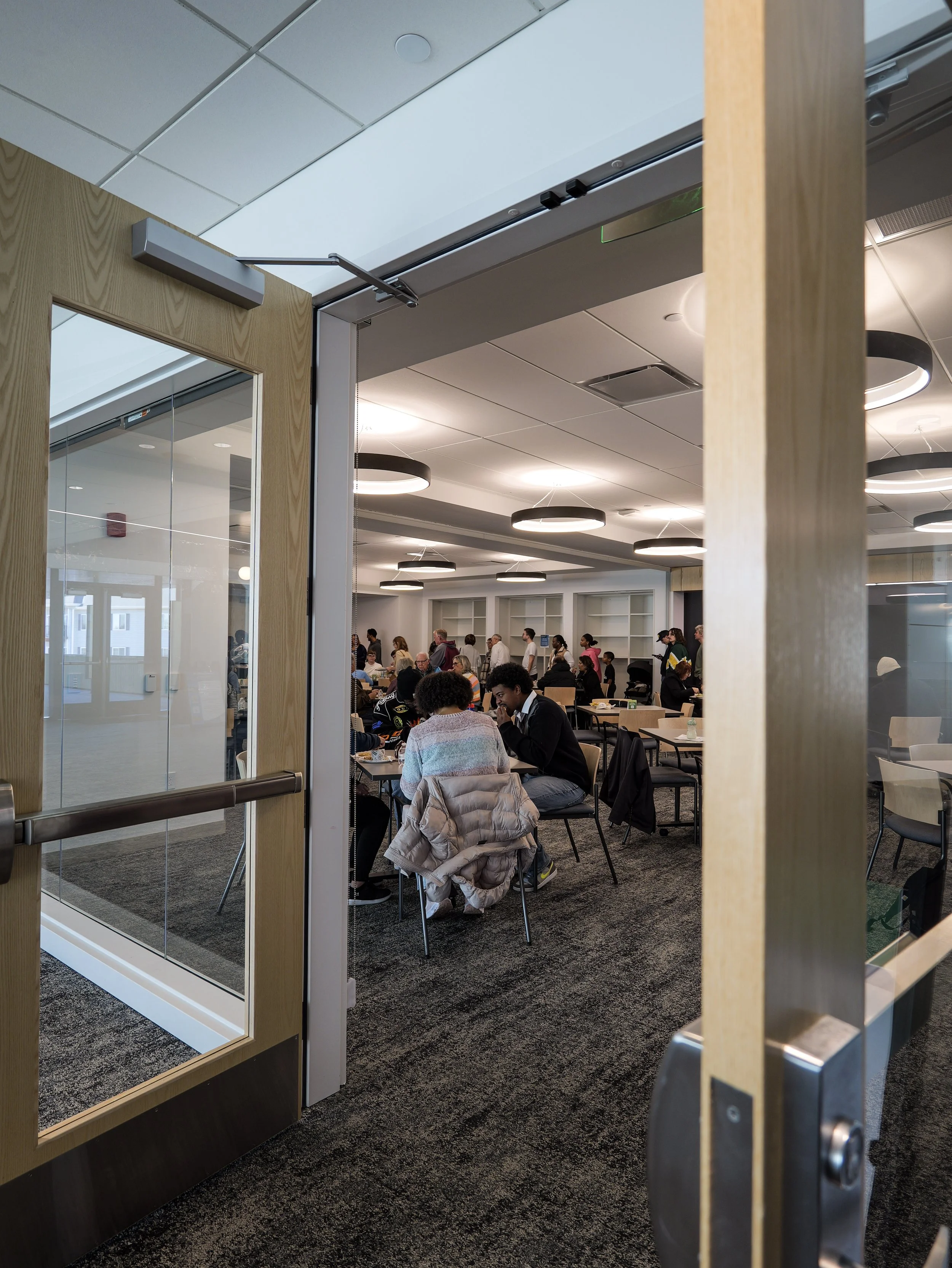 People seated at tables inside a bible study in Woodbury Minnesota, viewed through a partially open glass door with wooden framing.