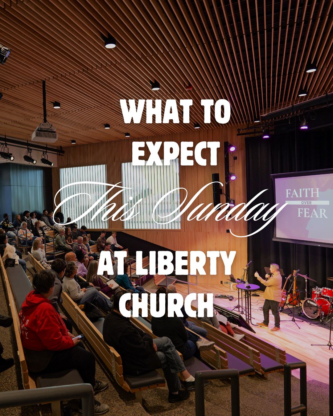 A church inside a modern auditorium with wooden ceiling panels, a congregation seated in pews, and a speaker on stage with a microphone, stage lights, and a large screen displaying 'FAITH OVER FEAR'. The overlay text says 'What to Expect This Sunday at Liberty Church.'