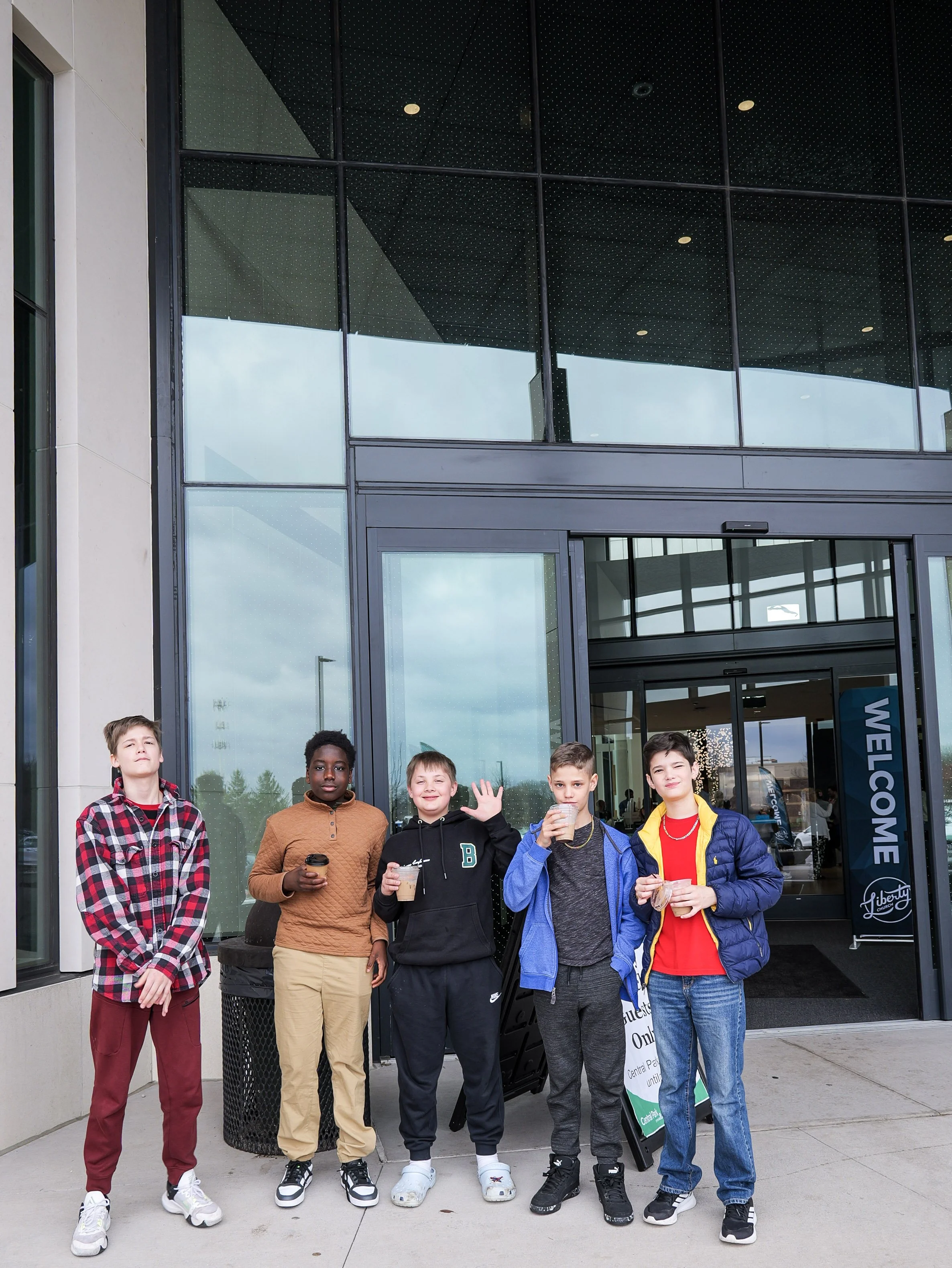 Young boys standing outside a church in Woodbury with glass windows, holding drinks and smiling.