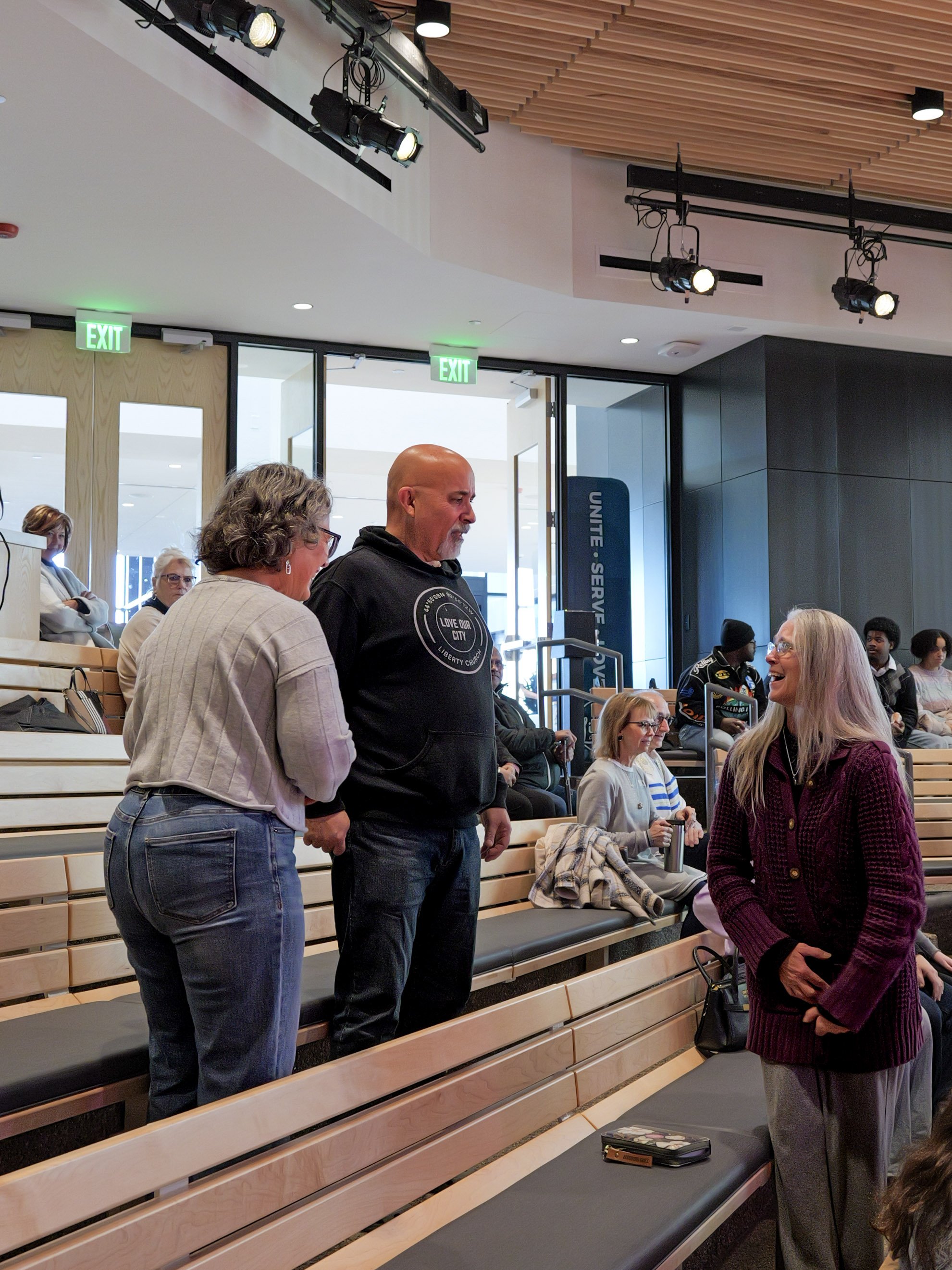 People sitting and standing in a modern church in Woodbury with wooden benches, talking and socializing.