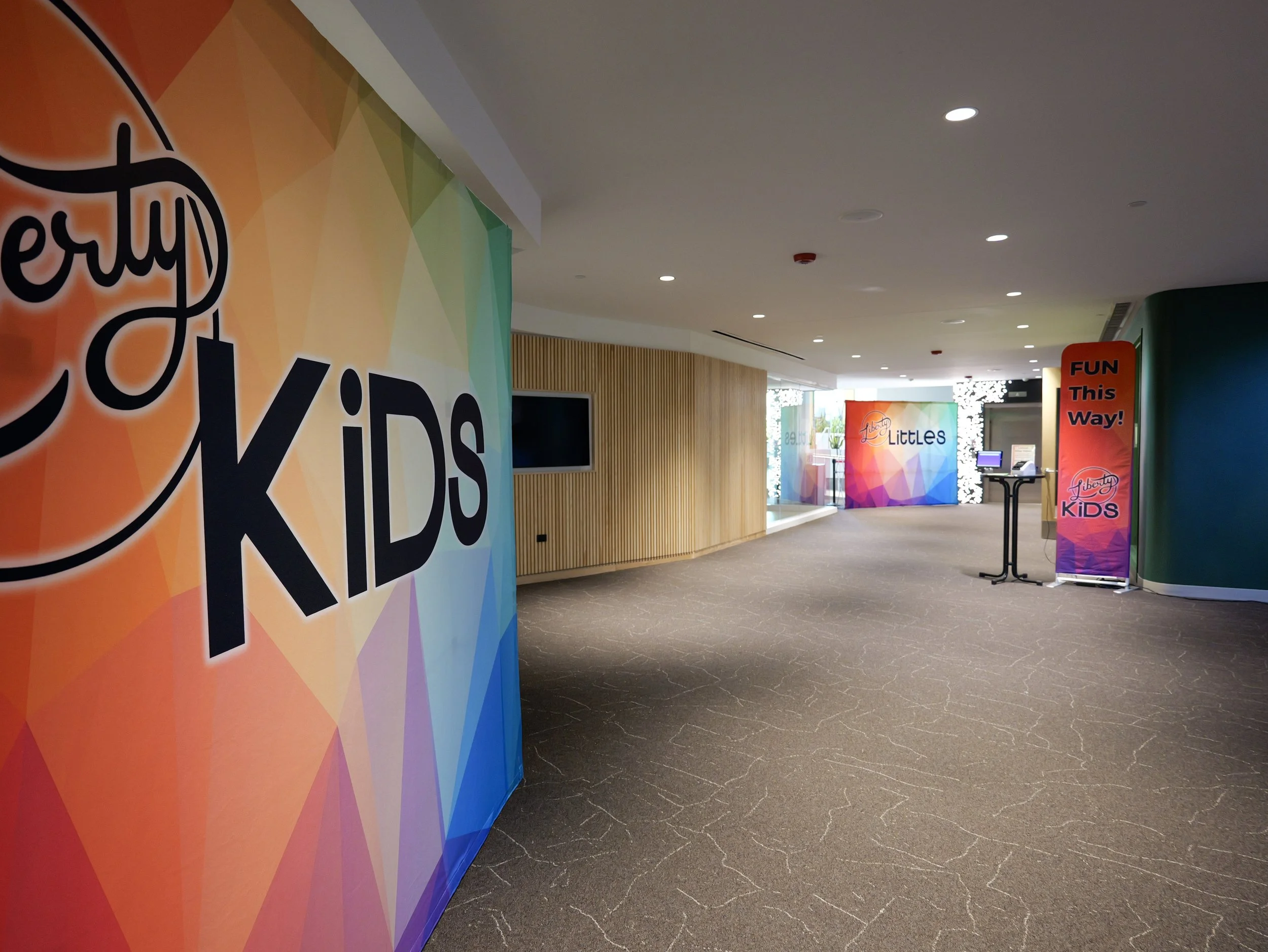 Interior of a colorful Kids' area at Liberty Church Woodbury with wall decorations and signs, including one that says "FUN! This Way!" and another that says "Liberty Littles".