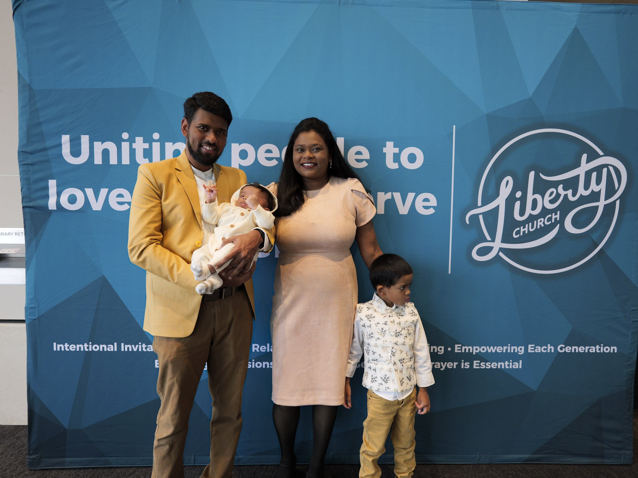 A family of four stands in front of a blue banner at a liberty church event. Smiling faces at a Christian community in Woodbury