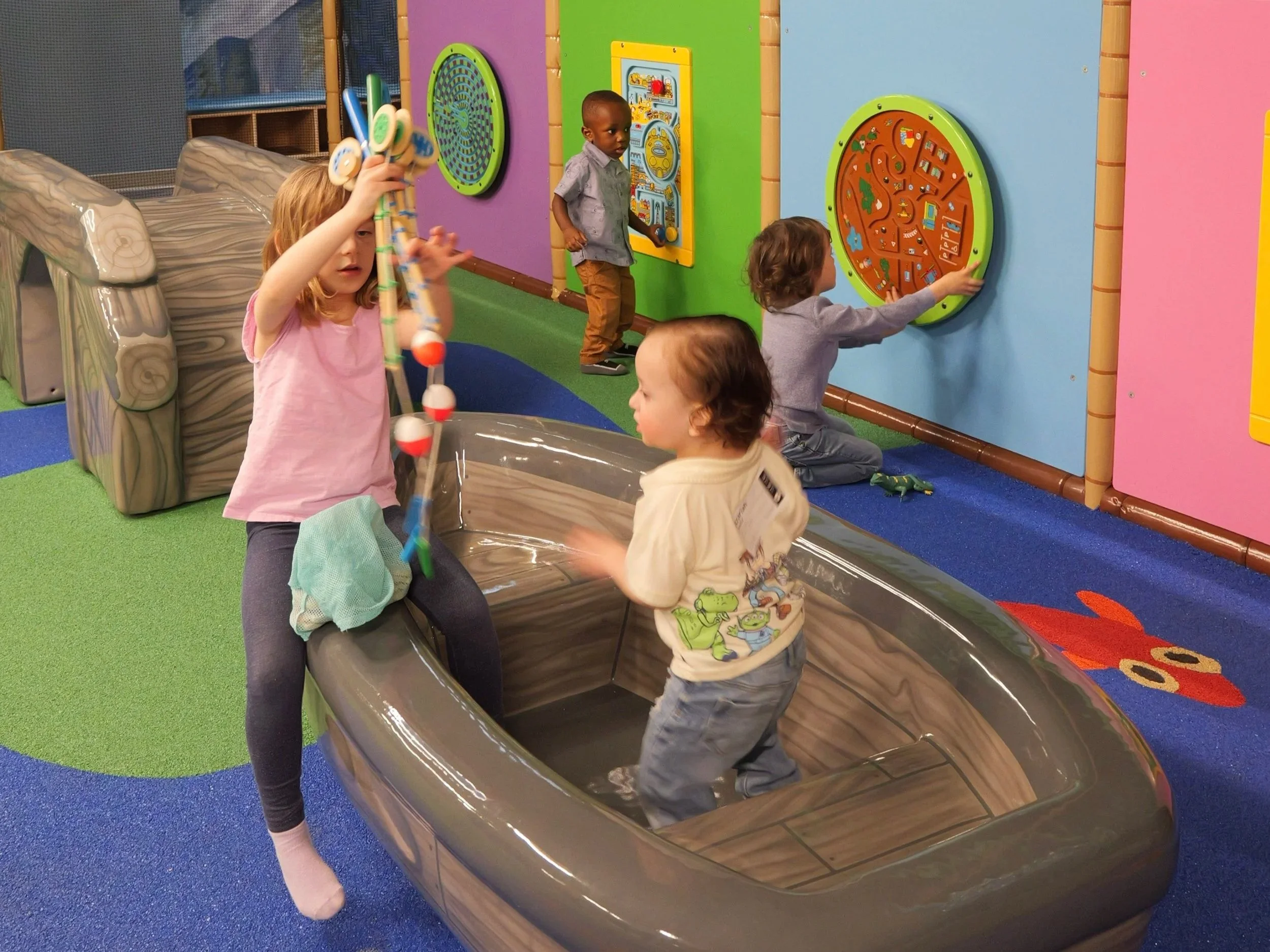 Children playing in an indoor play area with a small inflatable boat, colorful panels, and interactive wall activities where kids love to go to church at liberty church MN