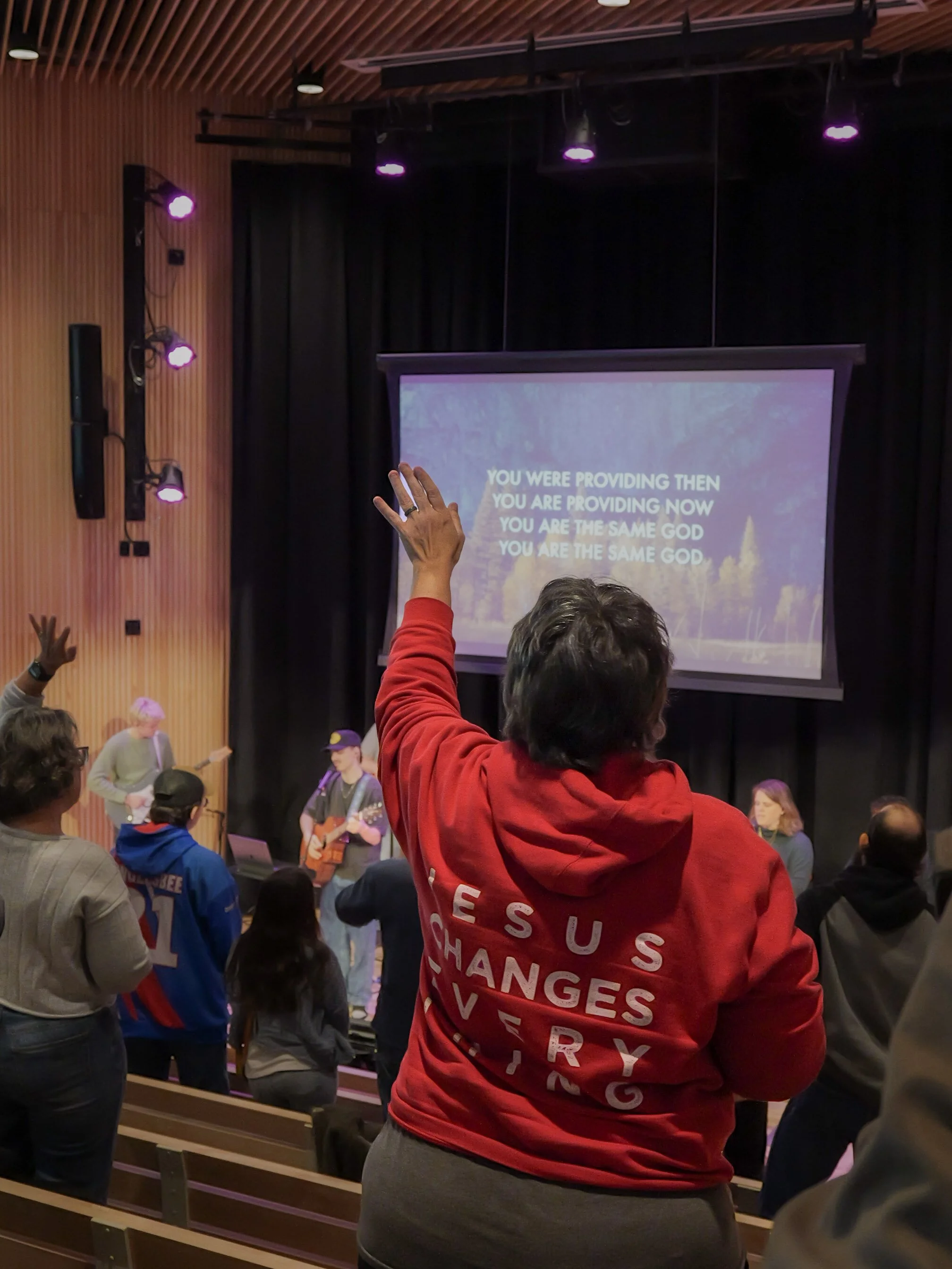 People raising their hands in a family church Minnesota with a screen displaying worship lyrics.