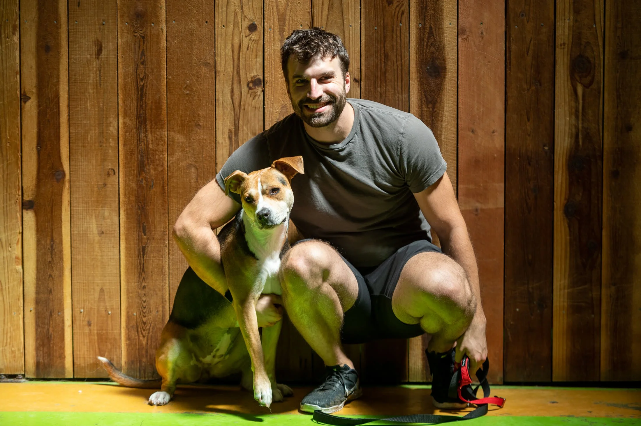A client crouching with his dog against the wood wall at Dan Perata Training in San Francisco