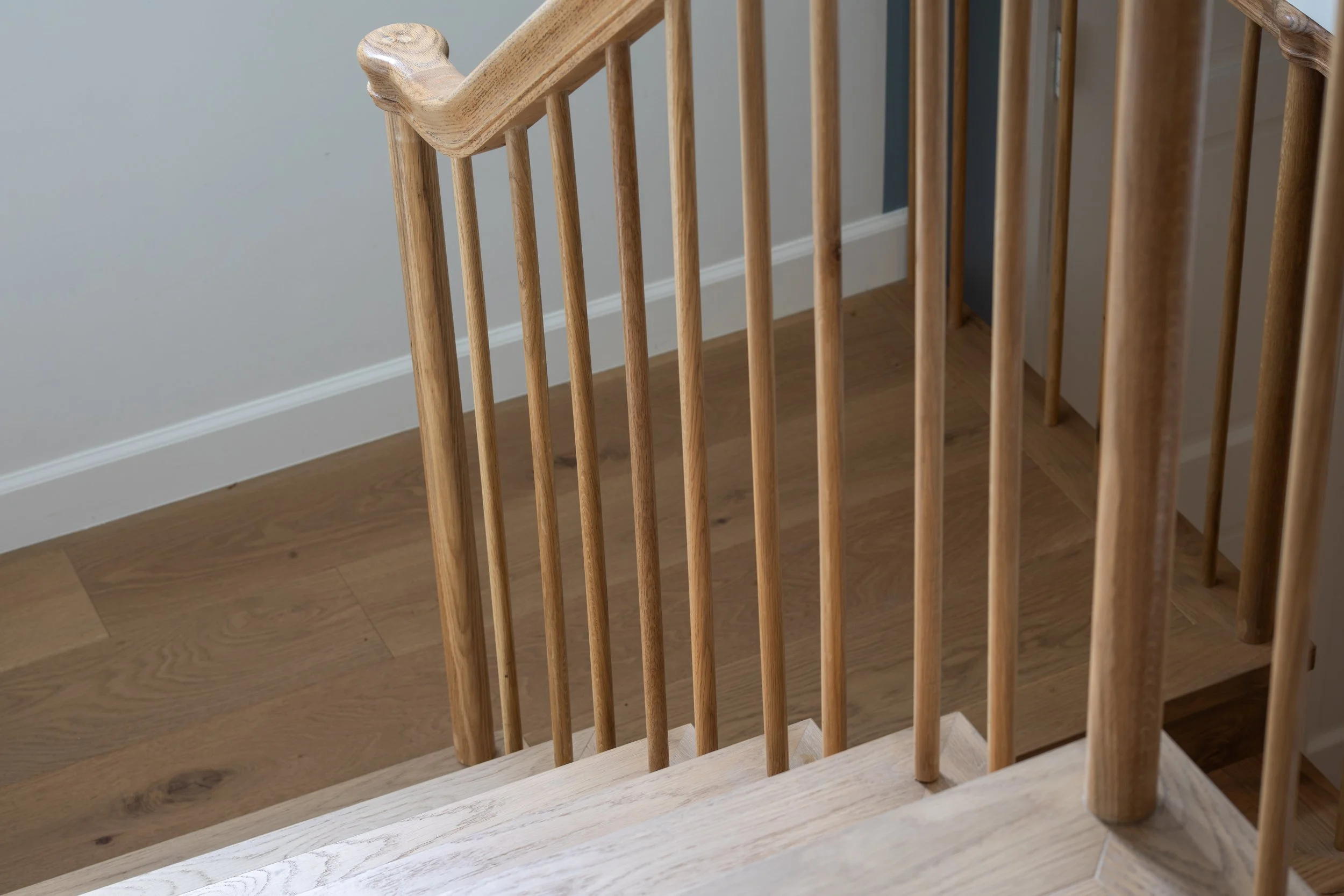 Wooden staircase railing and banister with light wood flooring and a wall with white and blue colors in the background.