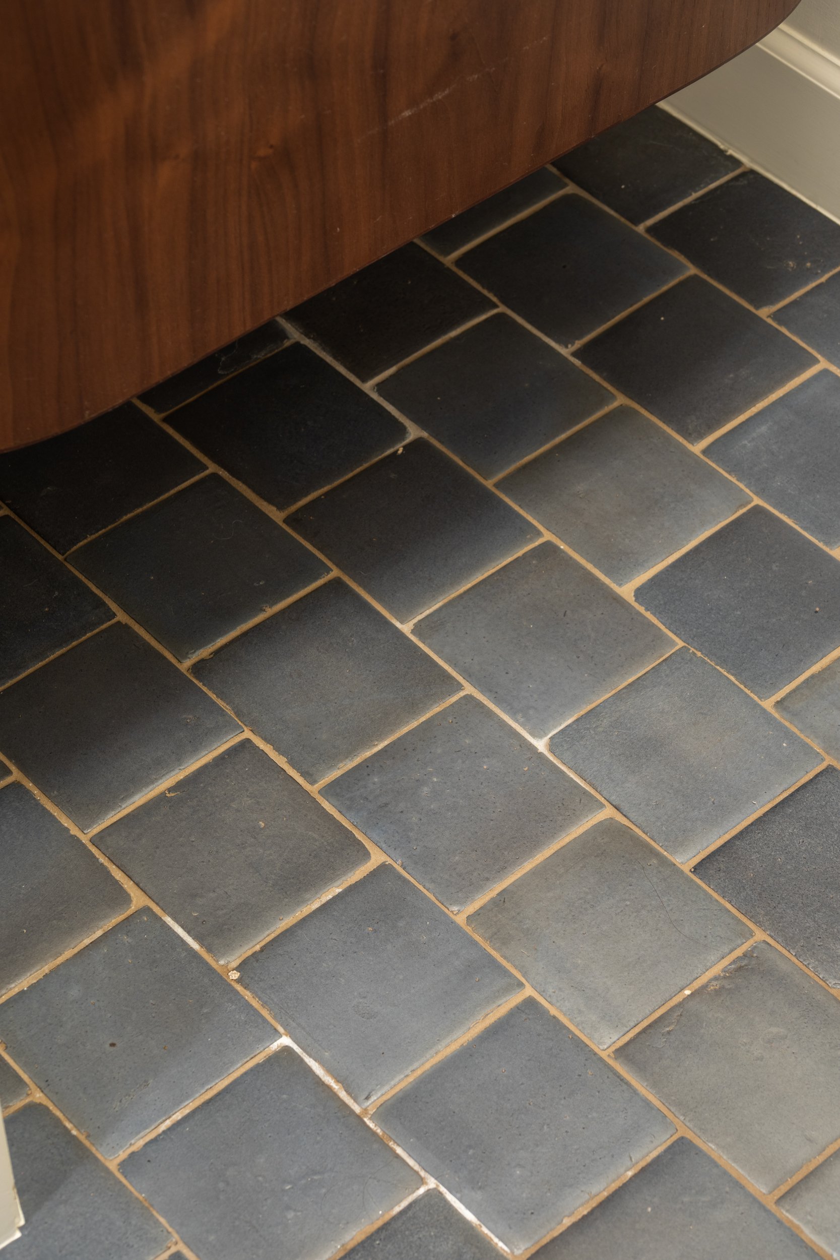 Close-up of a dark tiled floor with a wooden piece of furniture at the top of the image.