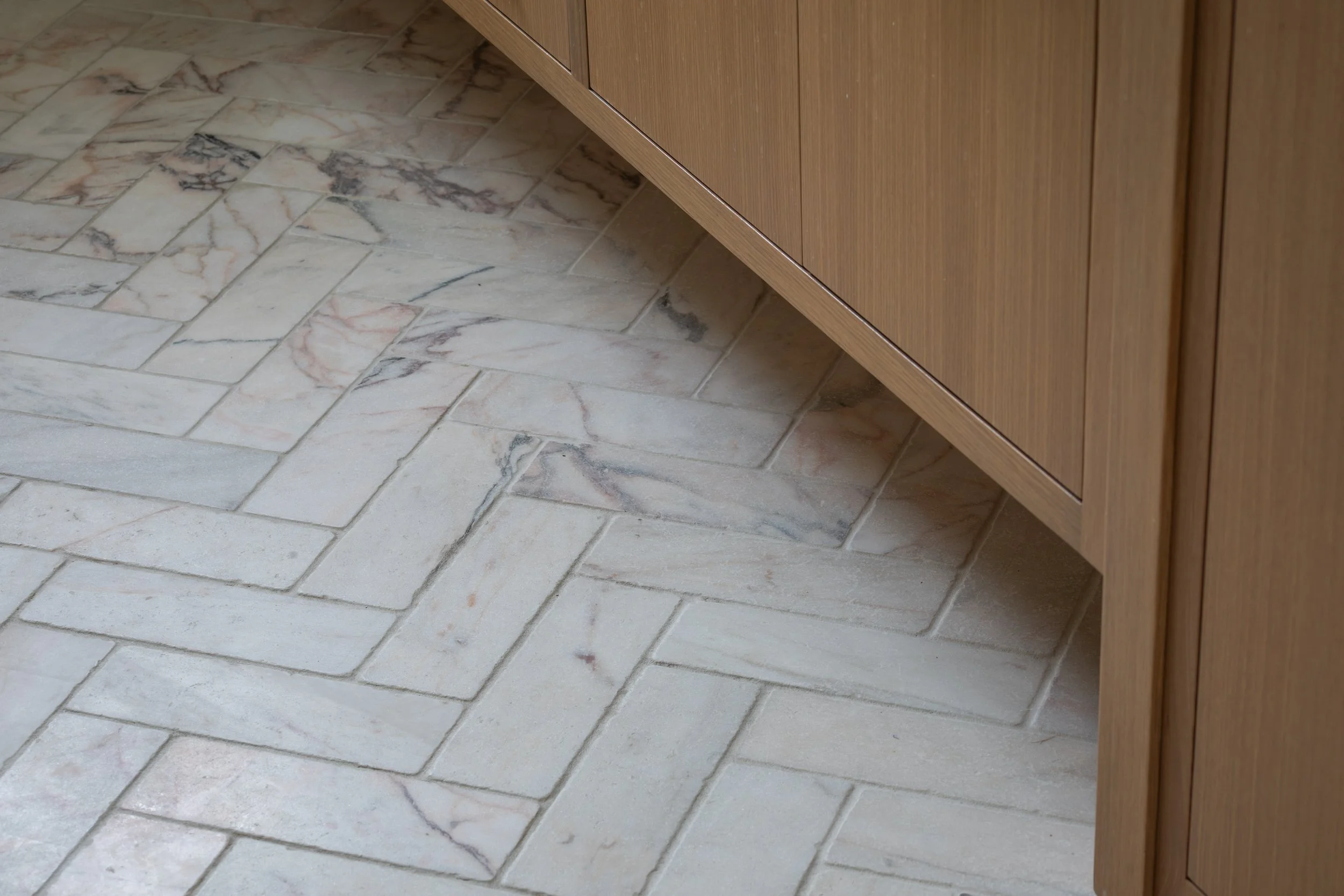 Close-up view of a kitchen floor with beige marble tiles and a wooden cabinet.