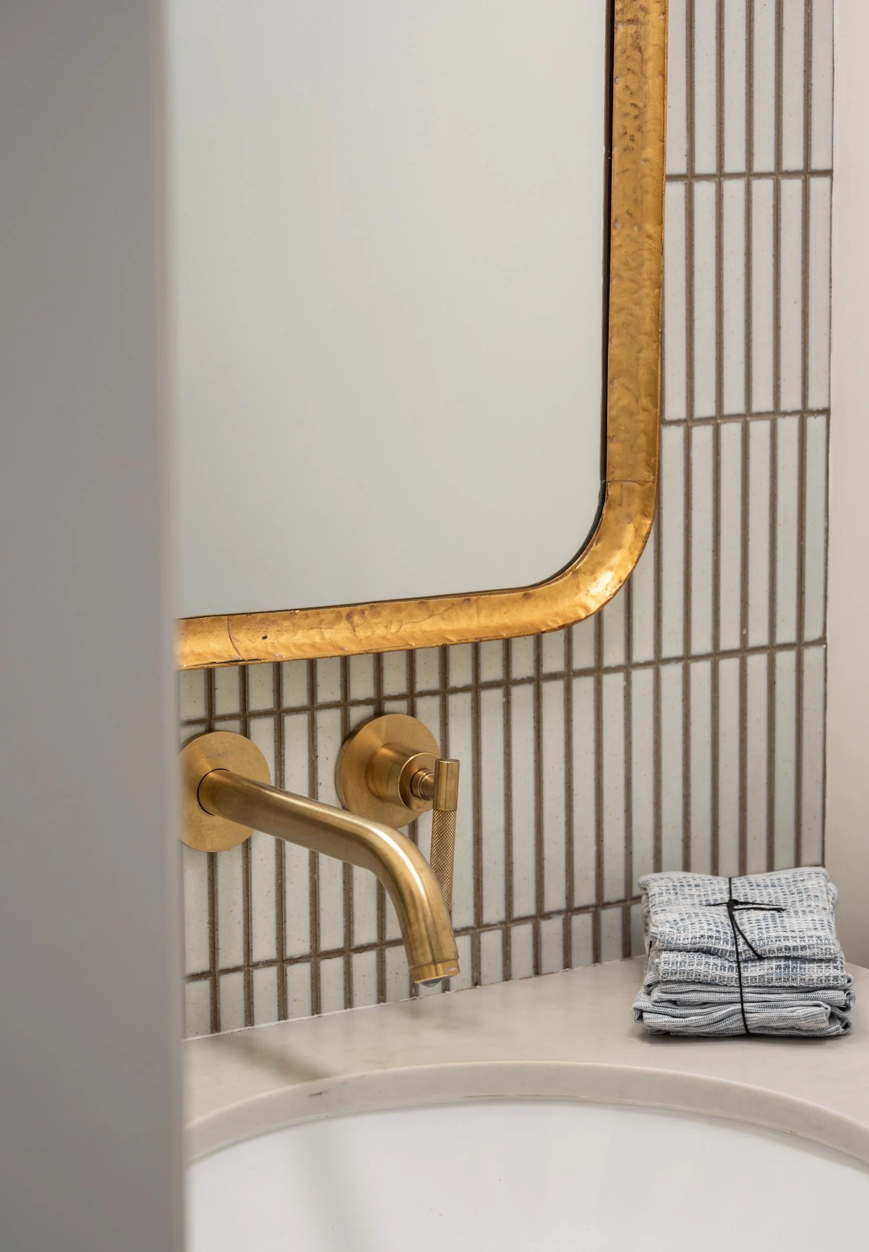 Bathroom sink area with a gold faucet, a decorative mirror, and a stack of folded towels on the countertop.