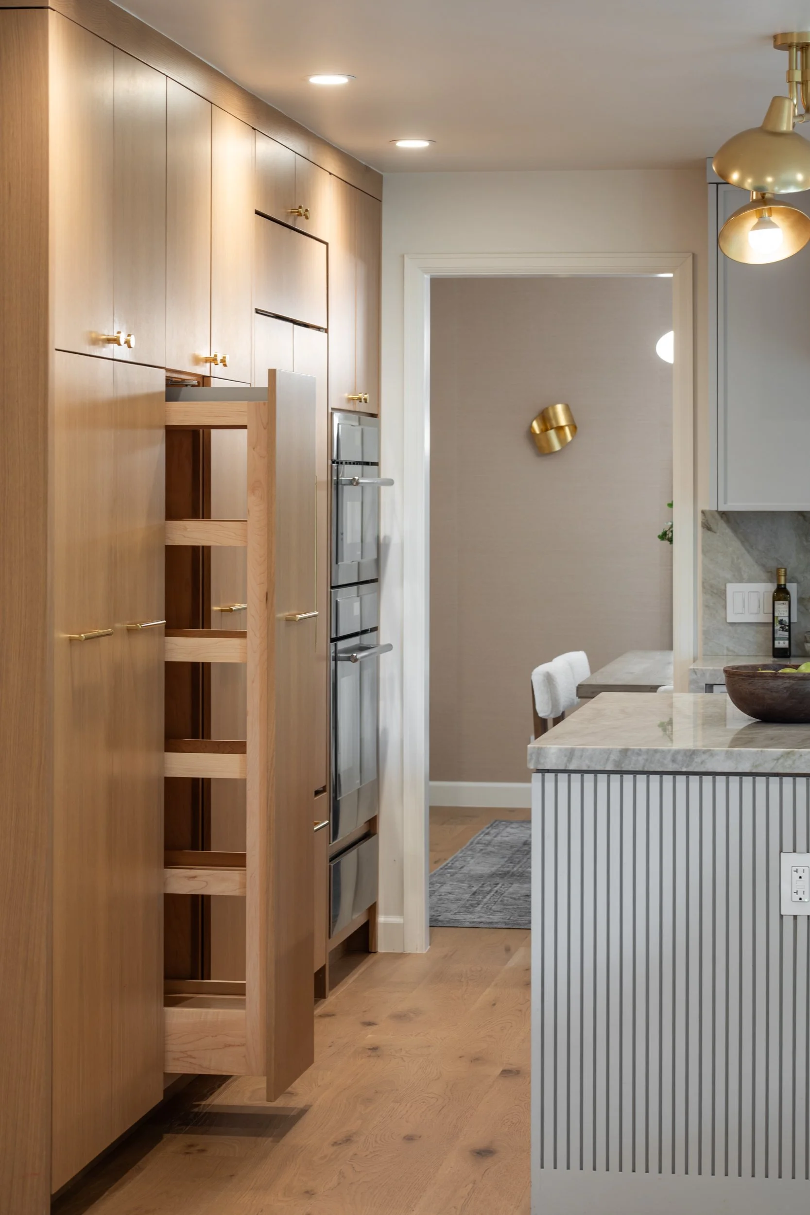 Kitchen with wooden cabinets, stainless steel appliances, and a dining area with a marble top table and white fabric chairs. Gold accents on light fixtures and wall decor. Hardwood flooring.