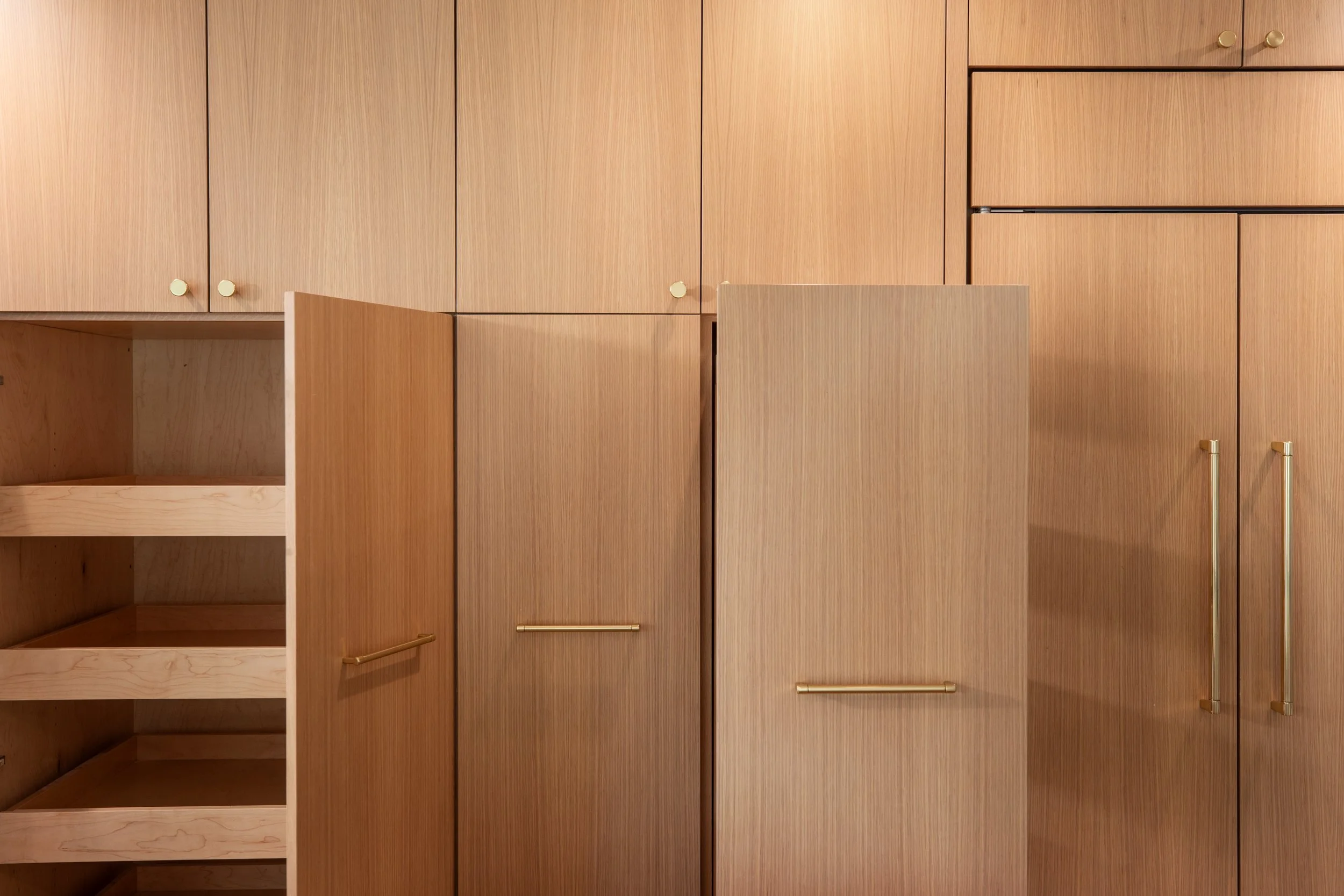 A wooden built-in cabinet with several closed doors and a few open shelves, with gold handles and knobs.