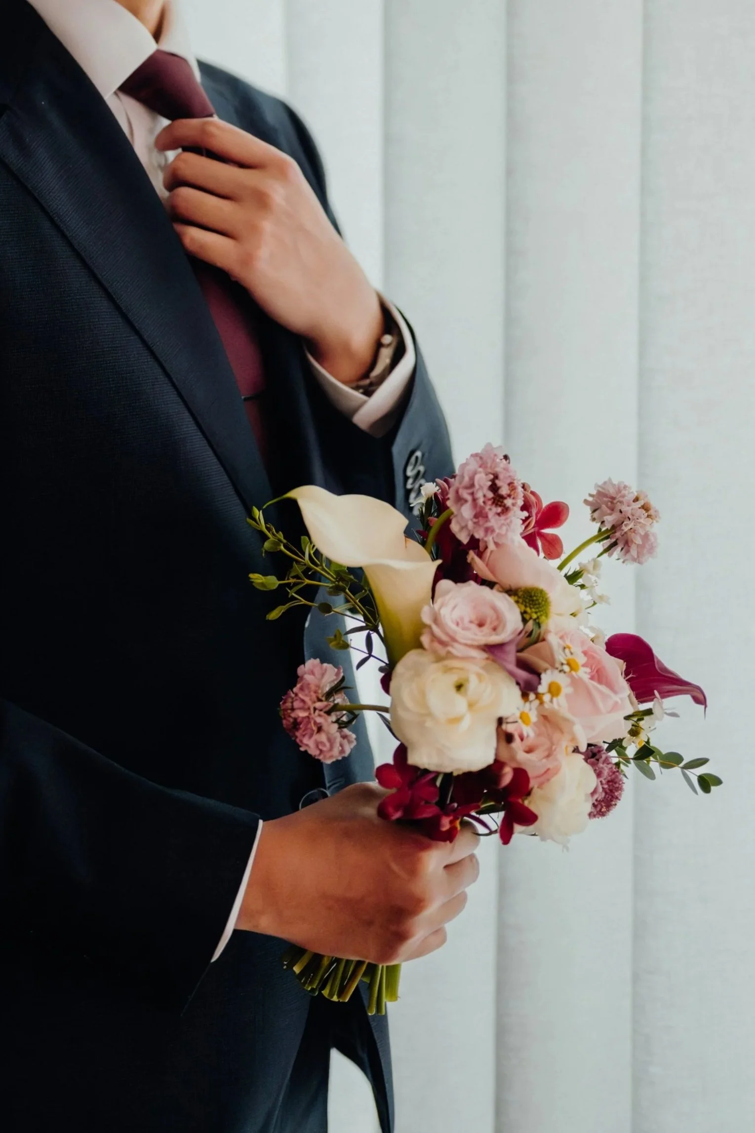 A person dressed in a suit and tie holding a bouquet of pink, white, and red flowers