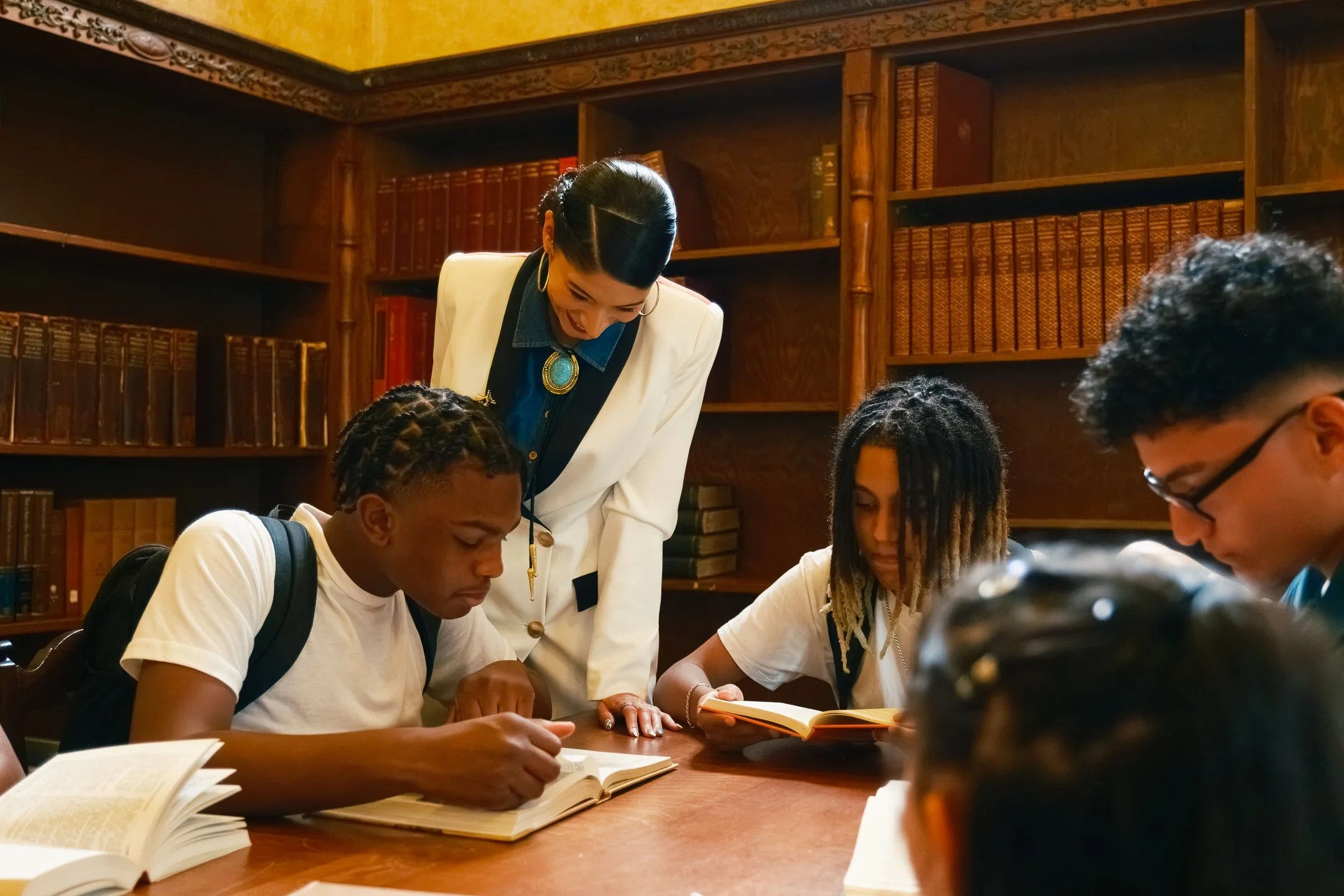 Mayra Valle working with high school students around a table in a library.