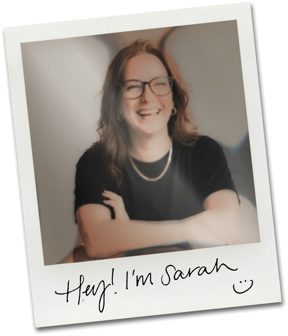 A woman with glasses and wavy brown hair smiling, wearing a black shirt and a pearl necklace, crossing her arms, with a handwritten note that says "Hey! I'm Sarah :)", on a Polaroid-style photo.