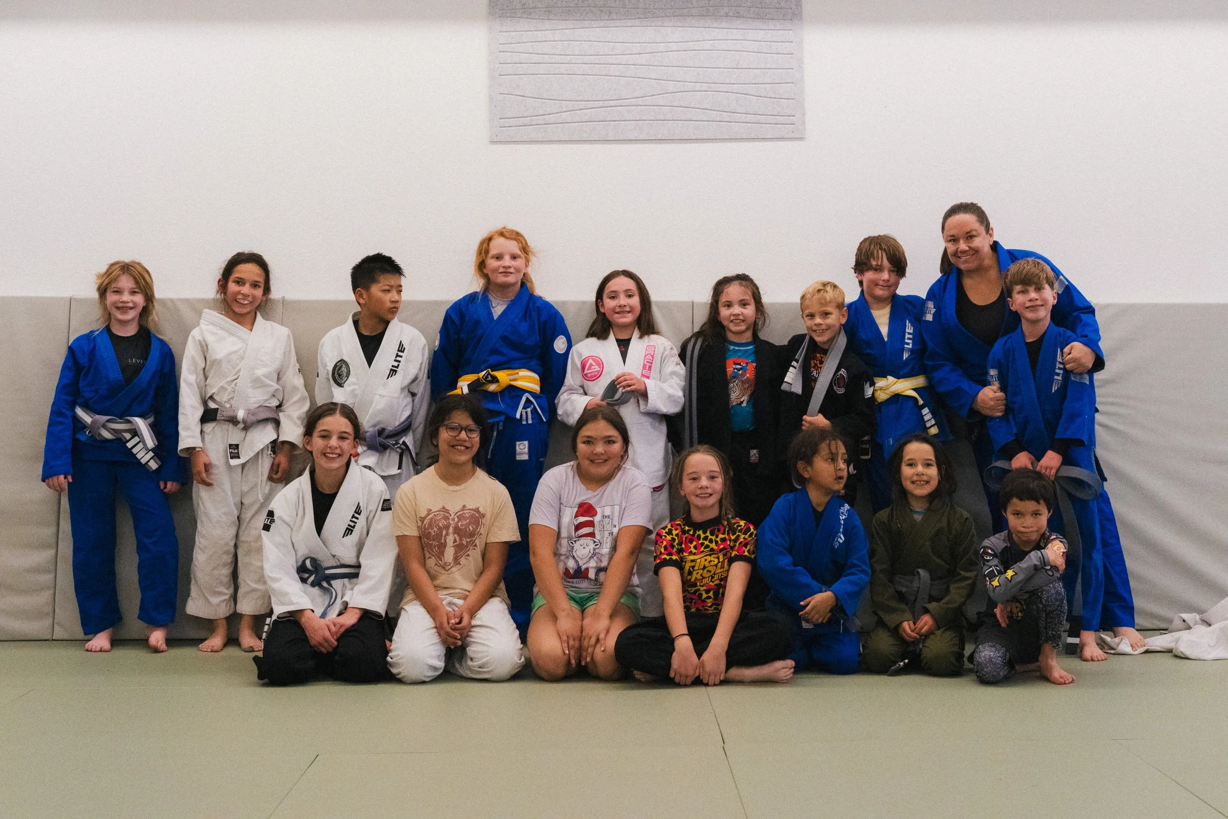 Group of children and a woman in martial arts uniforms posing together in a gym.

