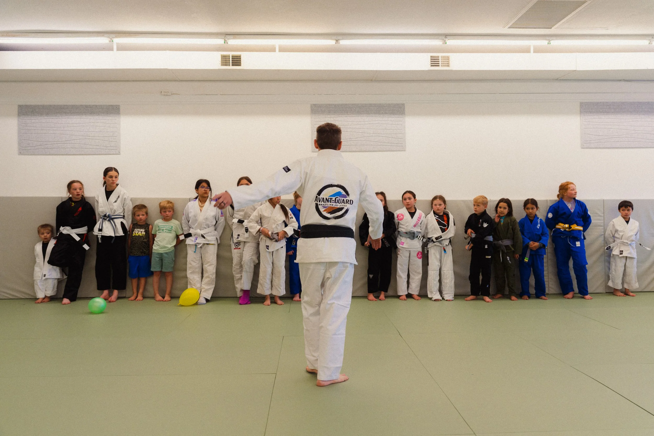 Martial arts instructor demonstrating techniques to children and teenagers in a gymnasium.