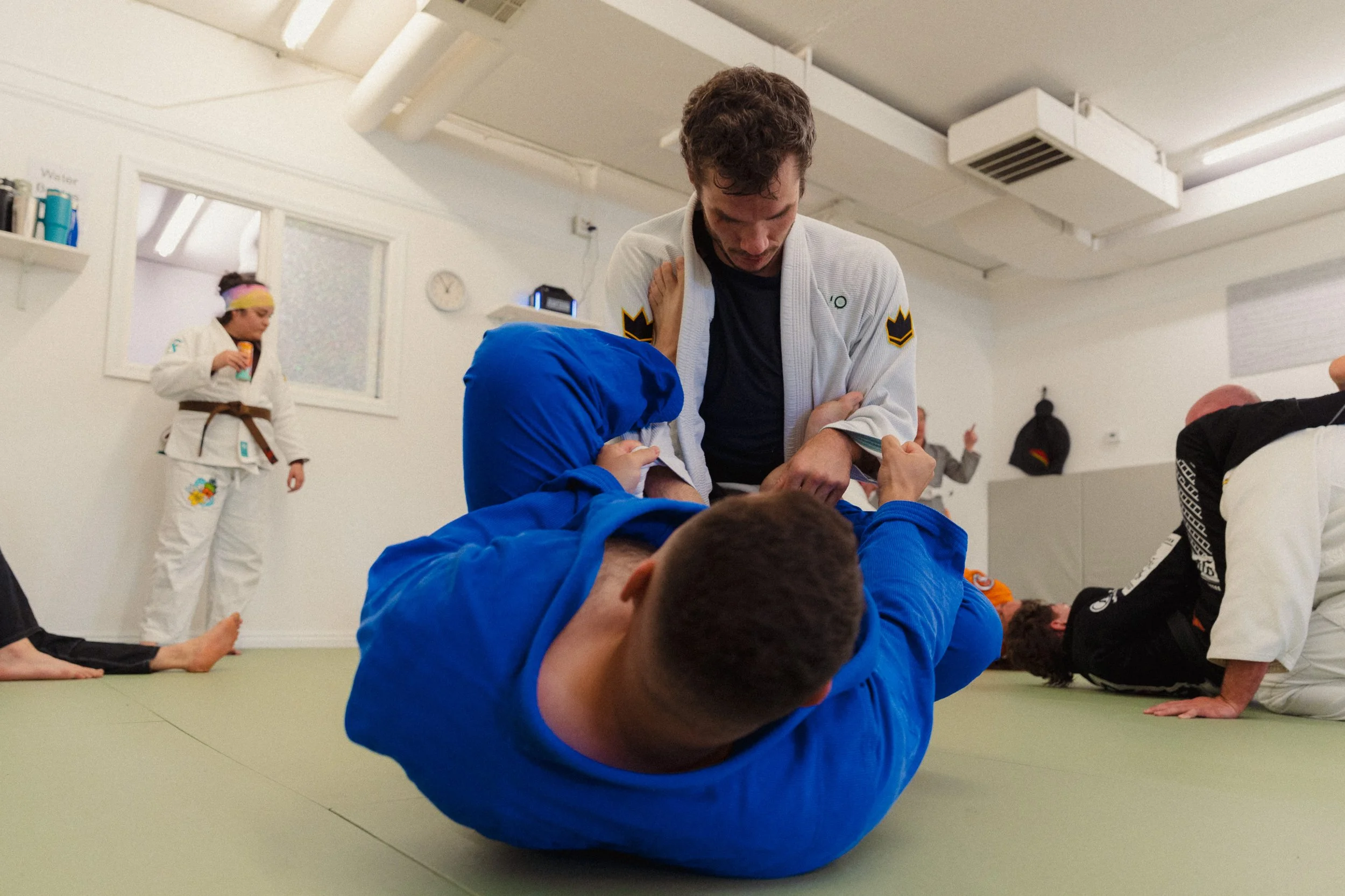 Martial arts class with students practicing techniques on mats; instructor assisting students in the background.