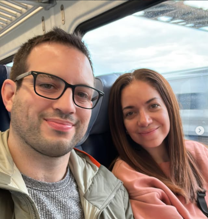 A man and woman sitting together on a train, smiling at the camera.
