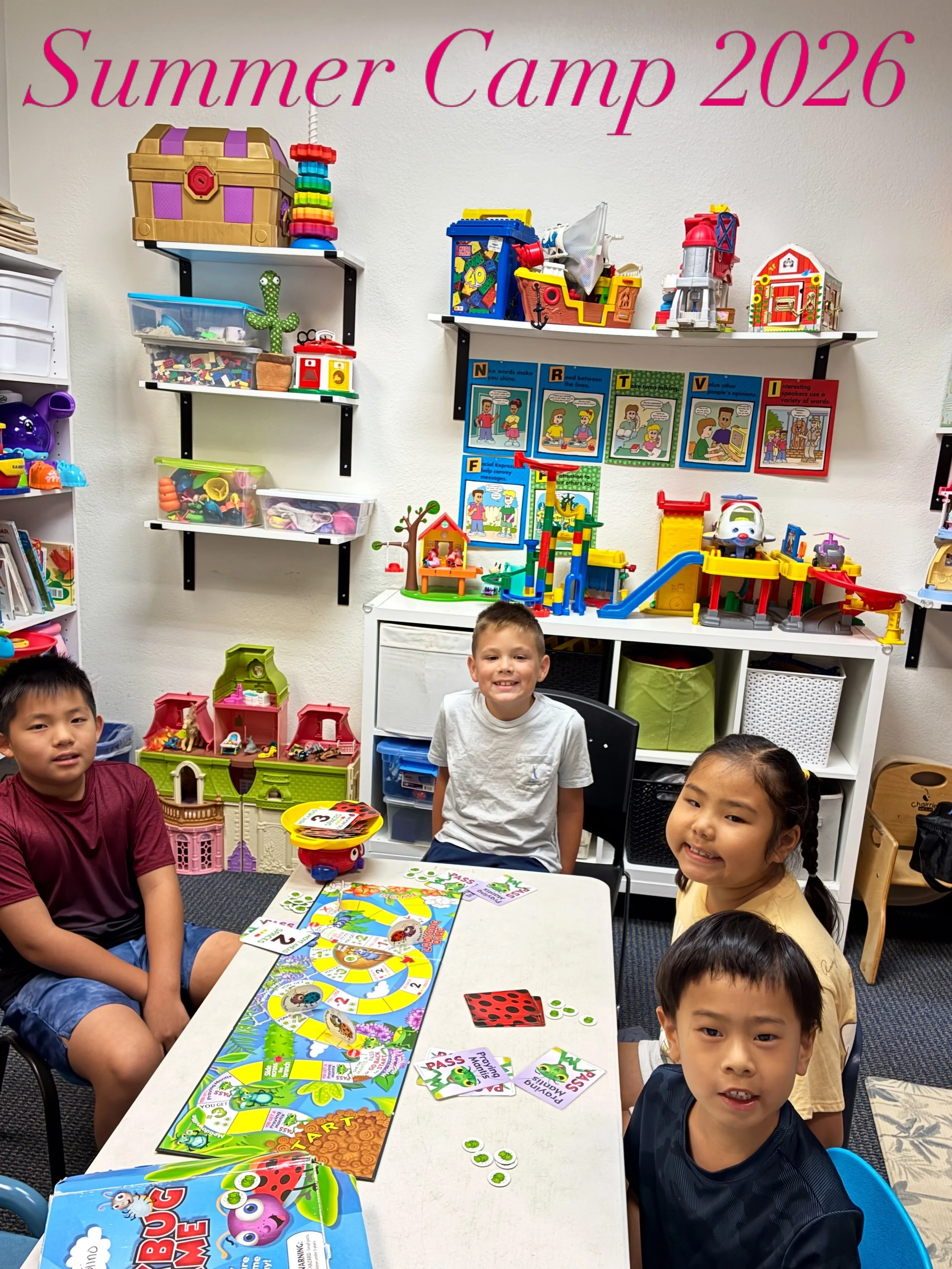 Children sitting around a table playing board games in a classroom, with toys and colorful decorations on shelves and posters on the wall that say "Summer Camp 2026."