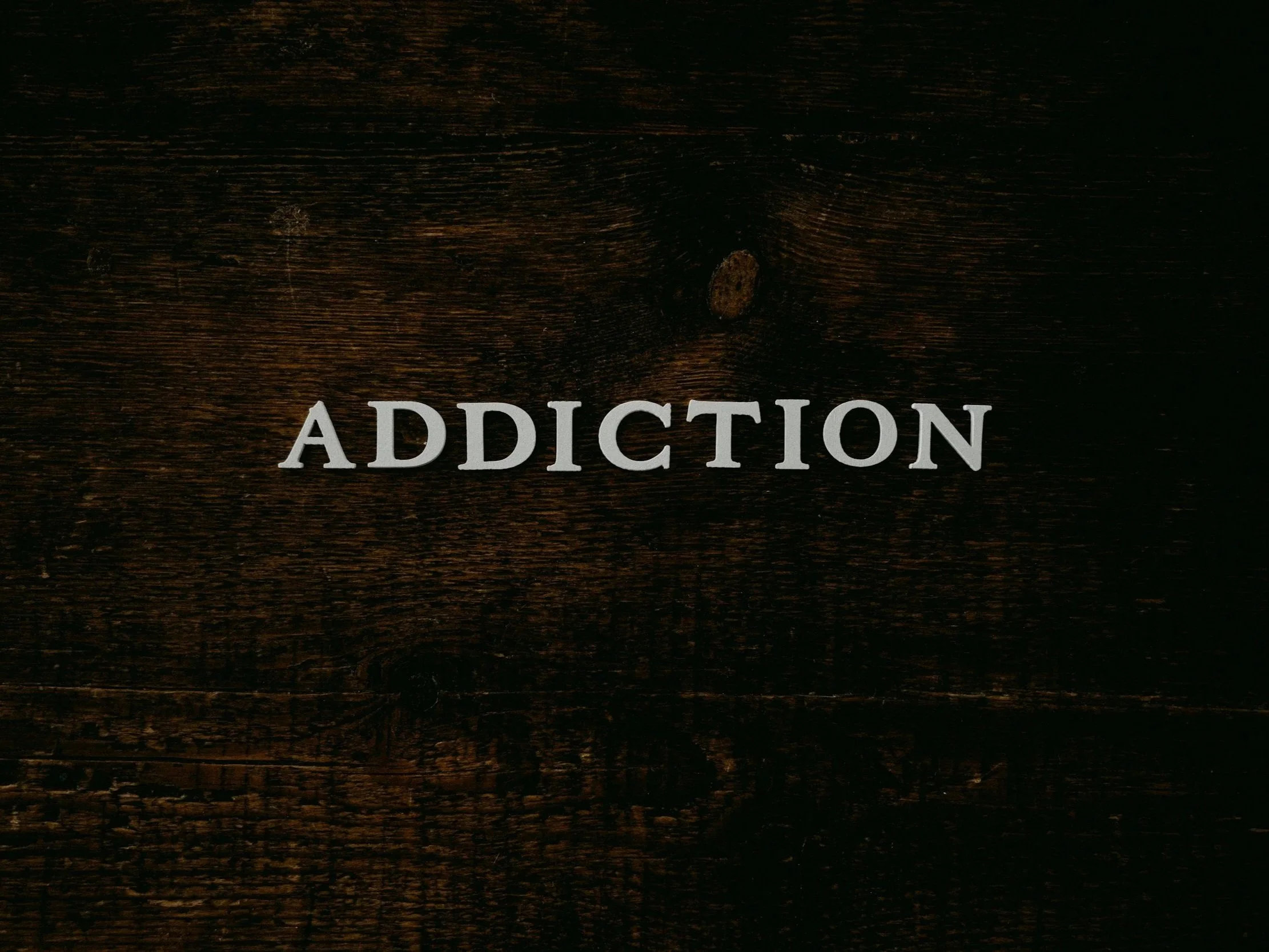 Close-up of a wooden surface with the word 'ADDICTION' written in bold, white, uppercase letters.