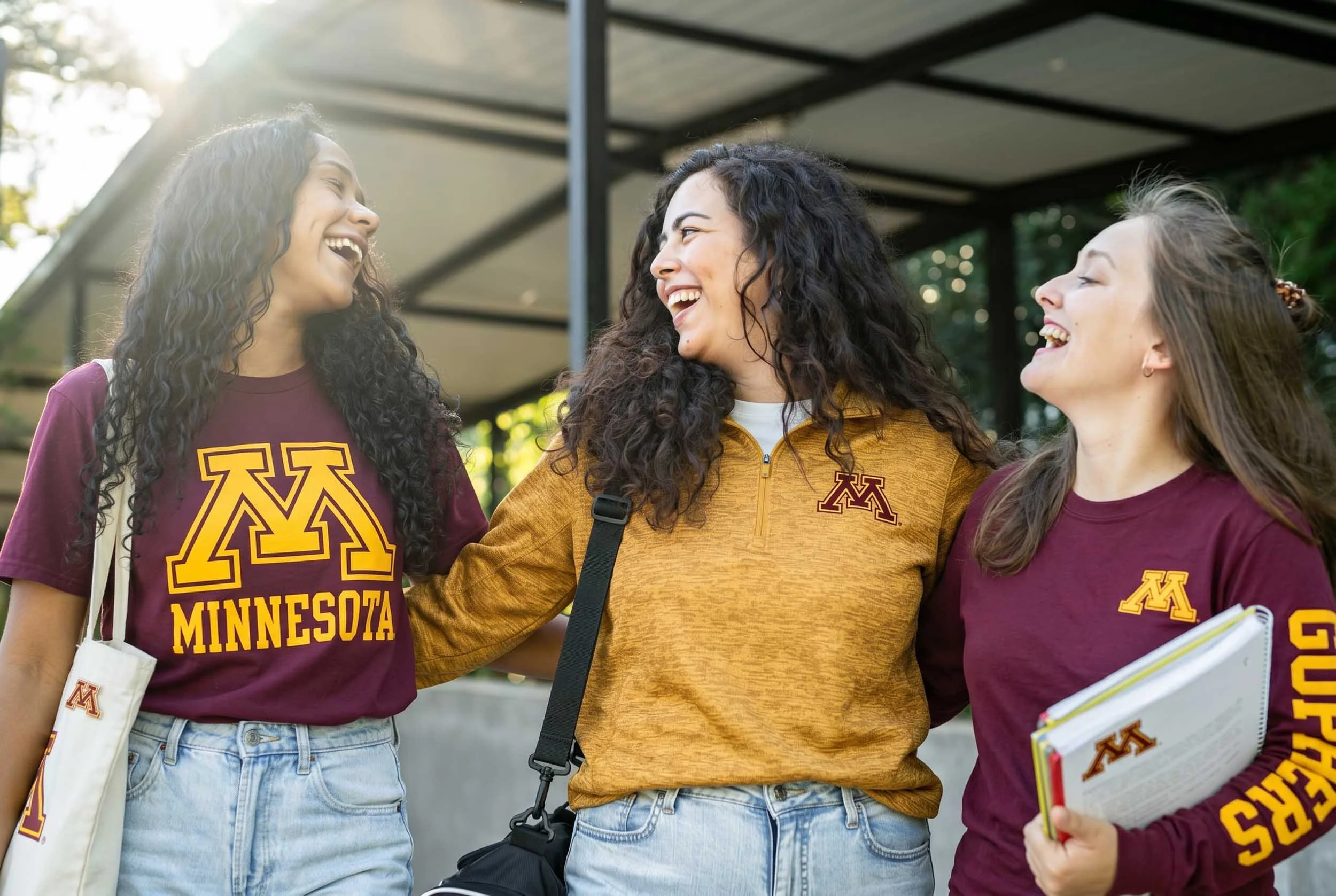 Three women standing outside, smiling and talking, wearing Minnesota Golden Gophers apparel.