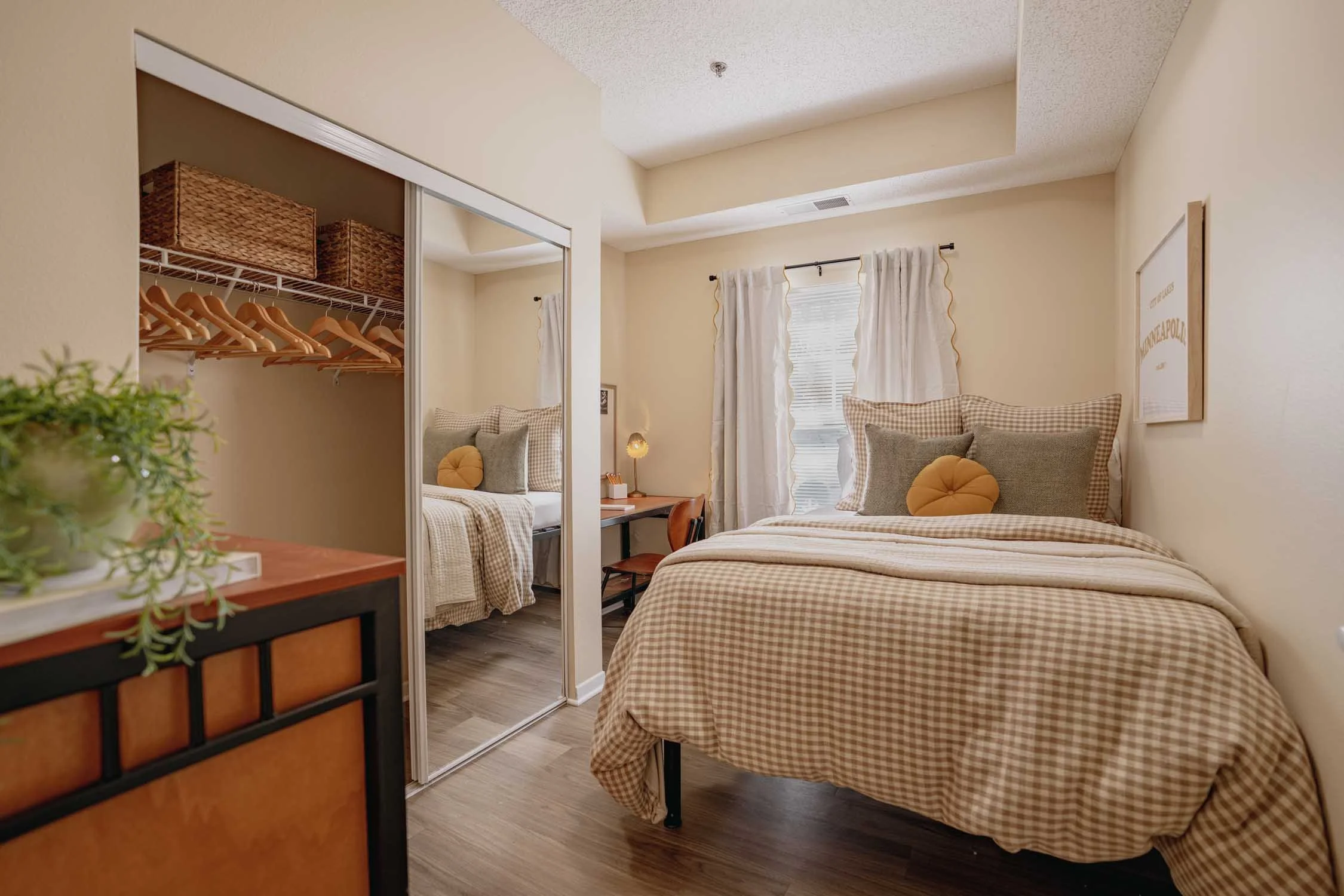 Cozy bedroom with a checkered bedspread, mirrored sliding-door closet, wicker storage baskets, desk, and window with white curtains