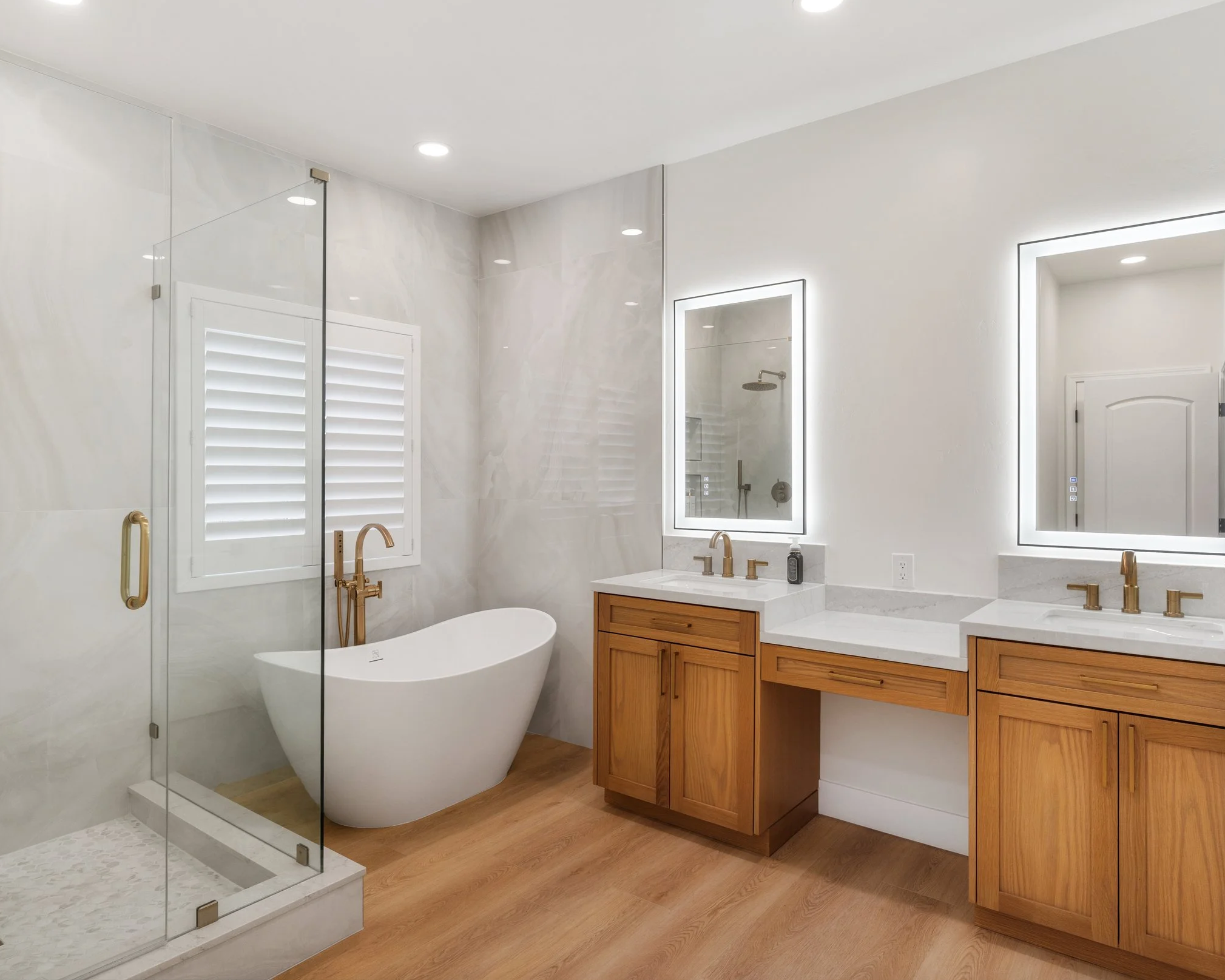 Modern bathroom with white walls, a freestanding bathtub, a glass shower enclosure, and wooden vanity cabinets with illuminated mirrors.