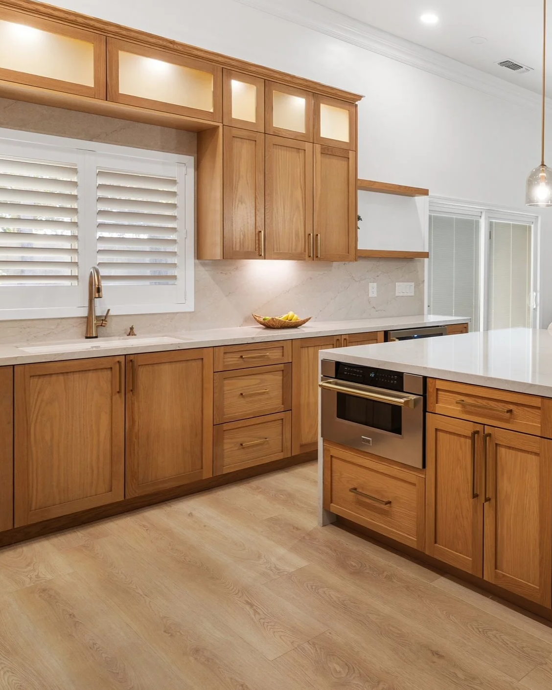 Kitchen with wooden cabinets, white countertops, a window with shutters, and a built-in oven.