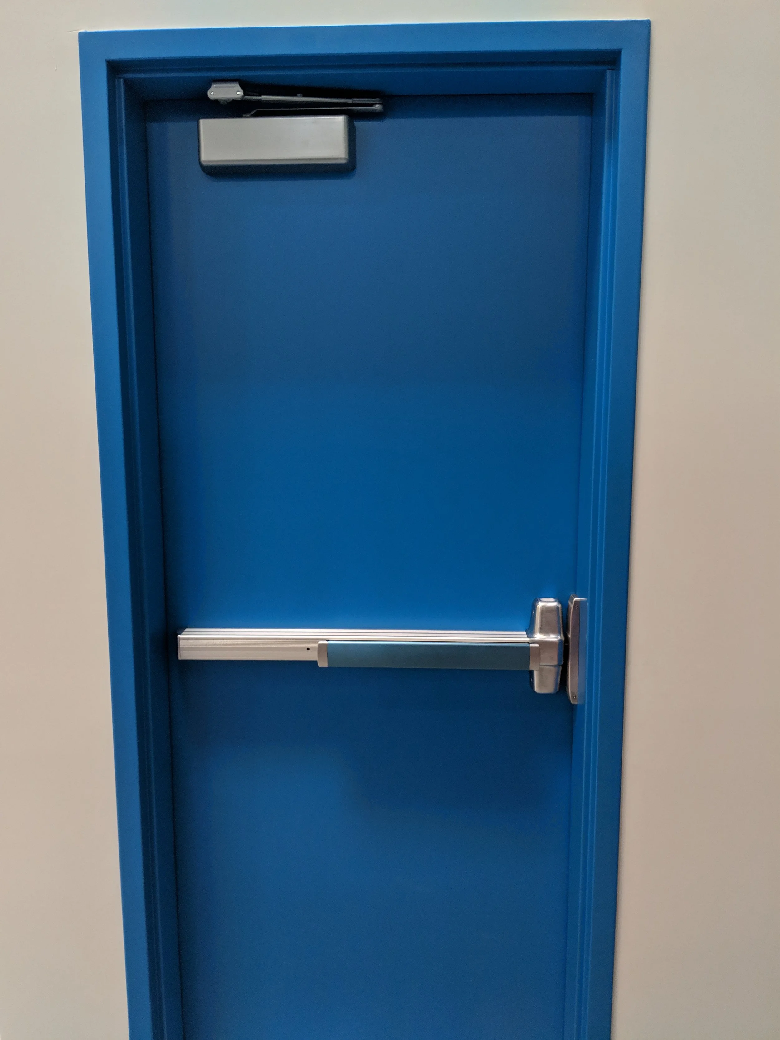 Blue fire door with a metal push bar handle and a door closer, set against a white wall.